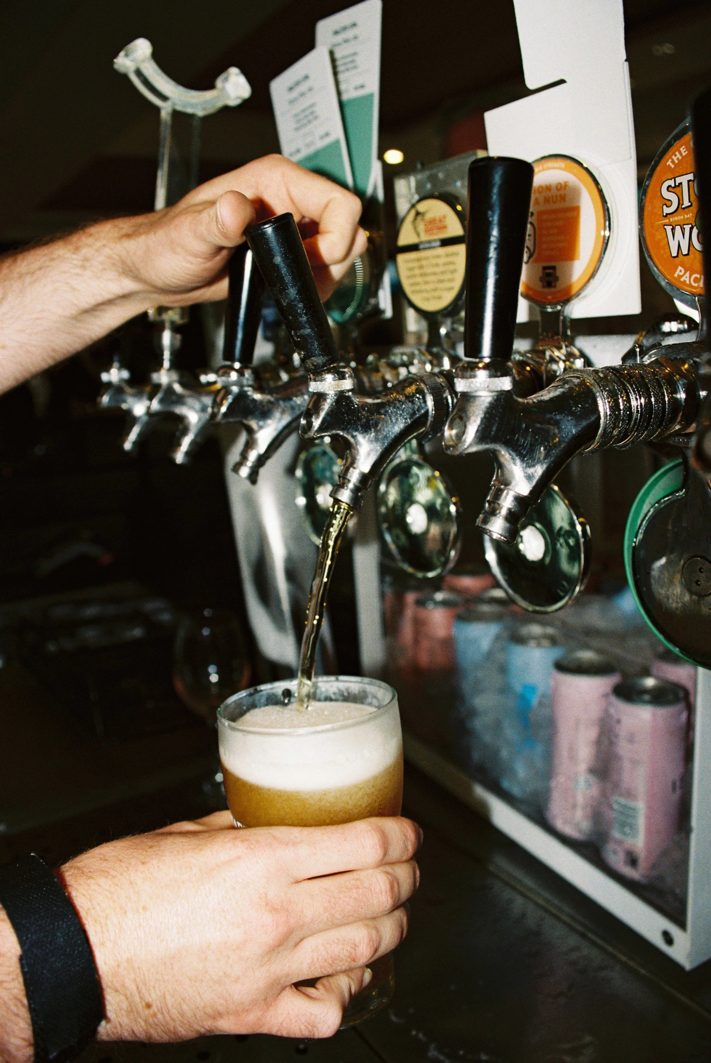 Person pouring beer from tap into glass at a bar or brewery.