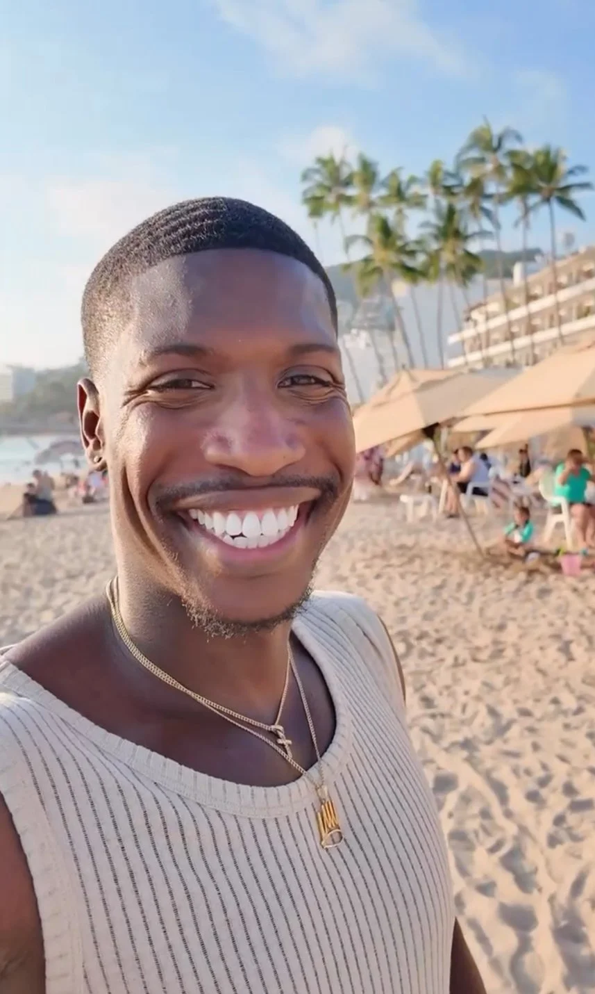Shane Samuel smiling on a beach in Puerto Vallarta, Mexico, with palm trees and a resort in the background.