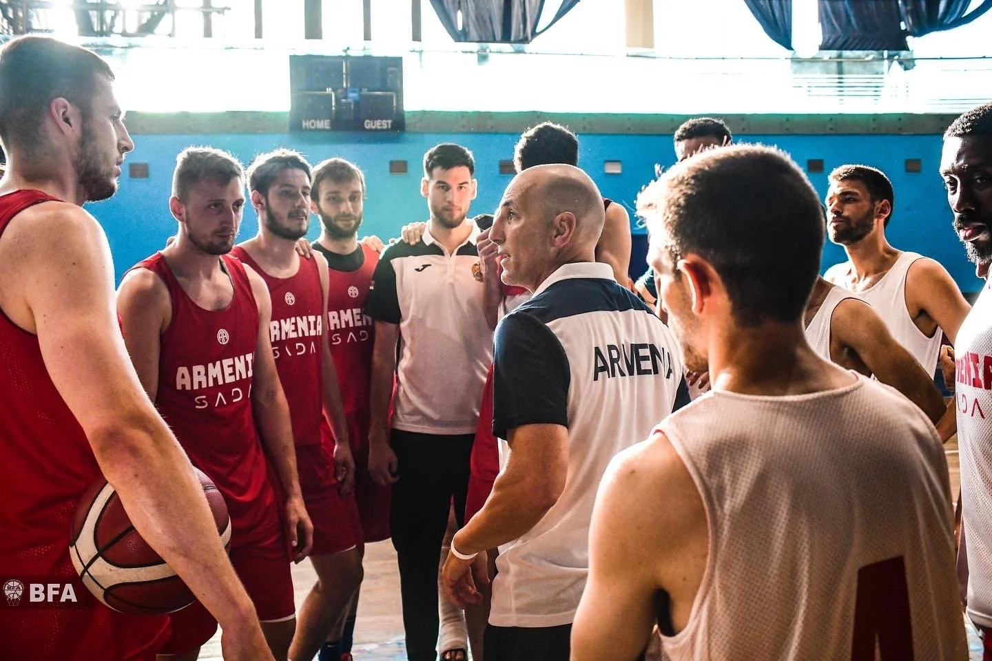 Basketball team huddle in gym with coach wearing 'ARMENIA' shirt