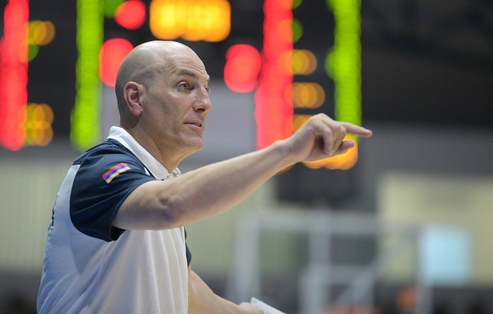 Coach giving instructions during a game with scoreboard in background.
