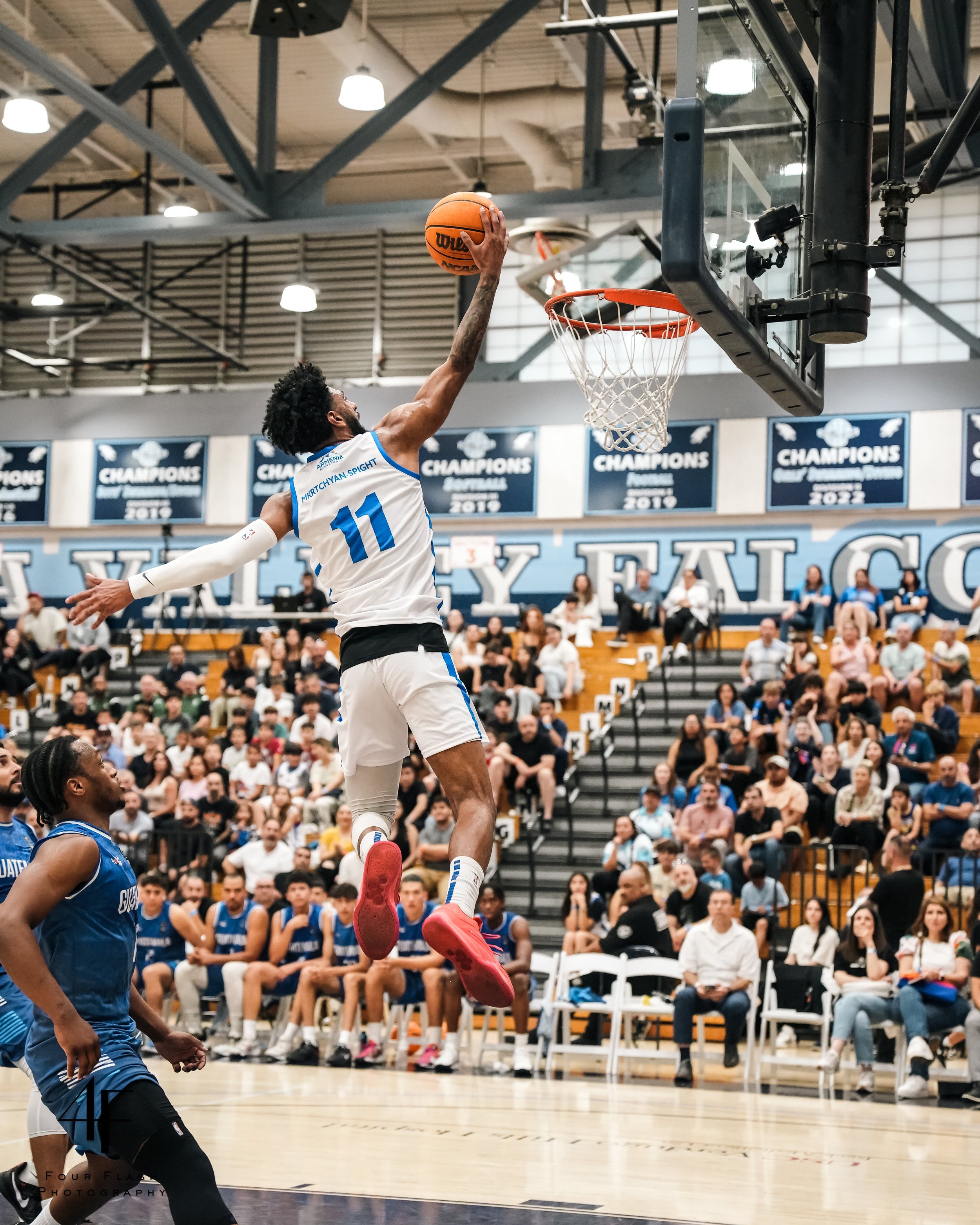 Basketball player in mid-air dunk, wearing number 11 jersey, crowded gymnasium, spectators watching.