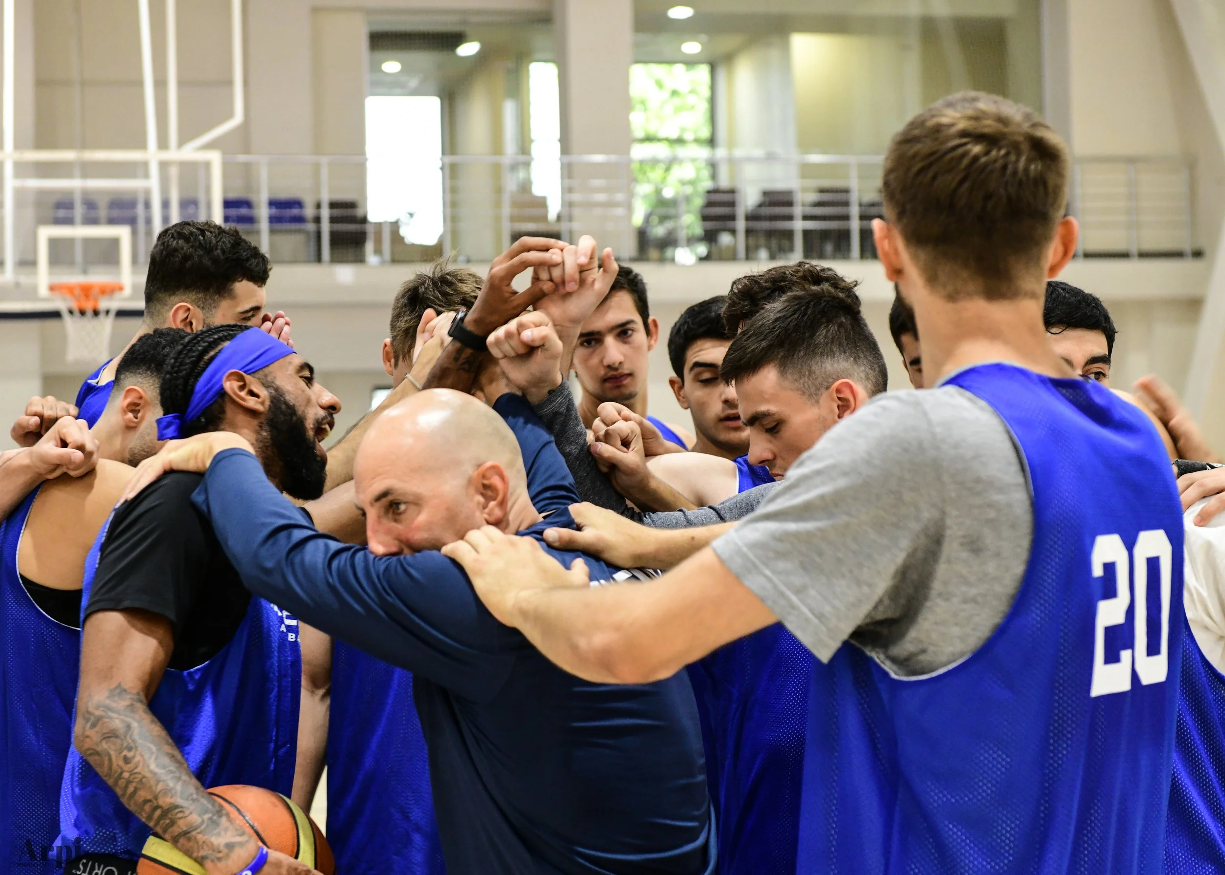 A basketball team in blue jerseys huddled together in a gym, showing unity and teamwork.
