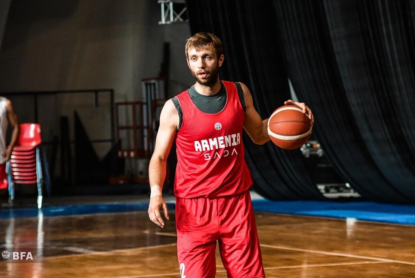 Basketball player in a red Armenia jersey holding a basketball on a court.