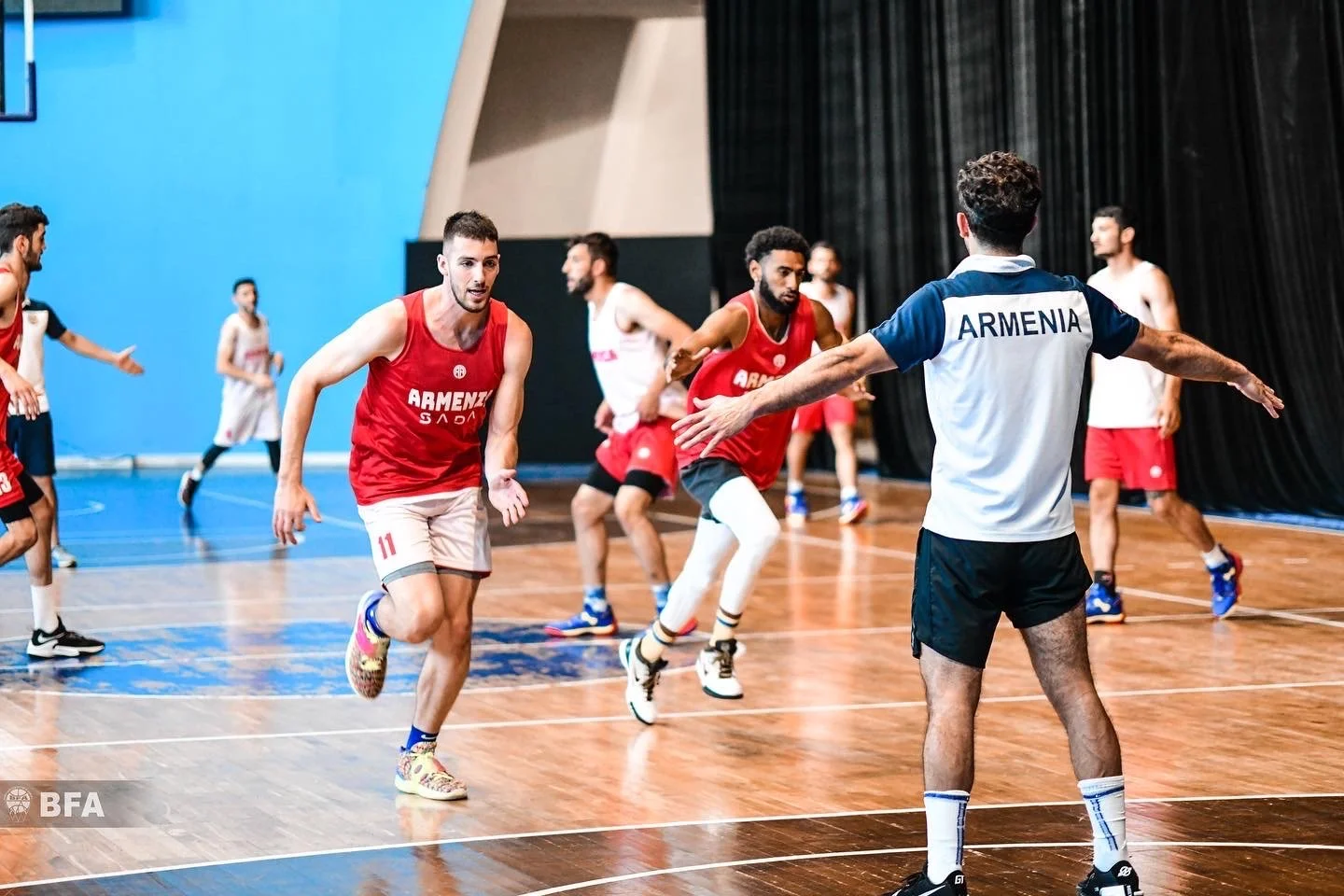 Basketball players in red and white jerseys practicing on an indoor court. One player wears a shirt labeled "Armenia."