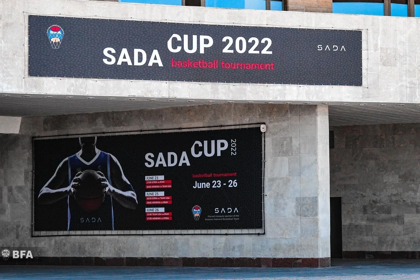 Entrance of a building displaying promotional banners for the SADA Cup 2022 basketball tournament, scheduled from June 23 to 26.