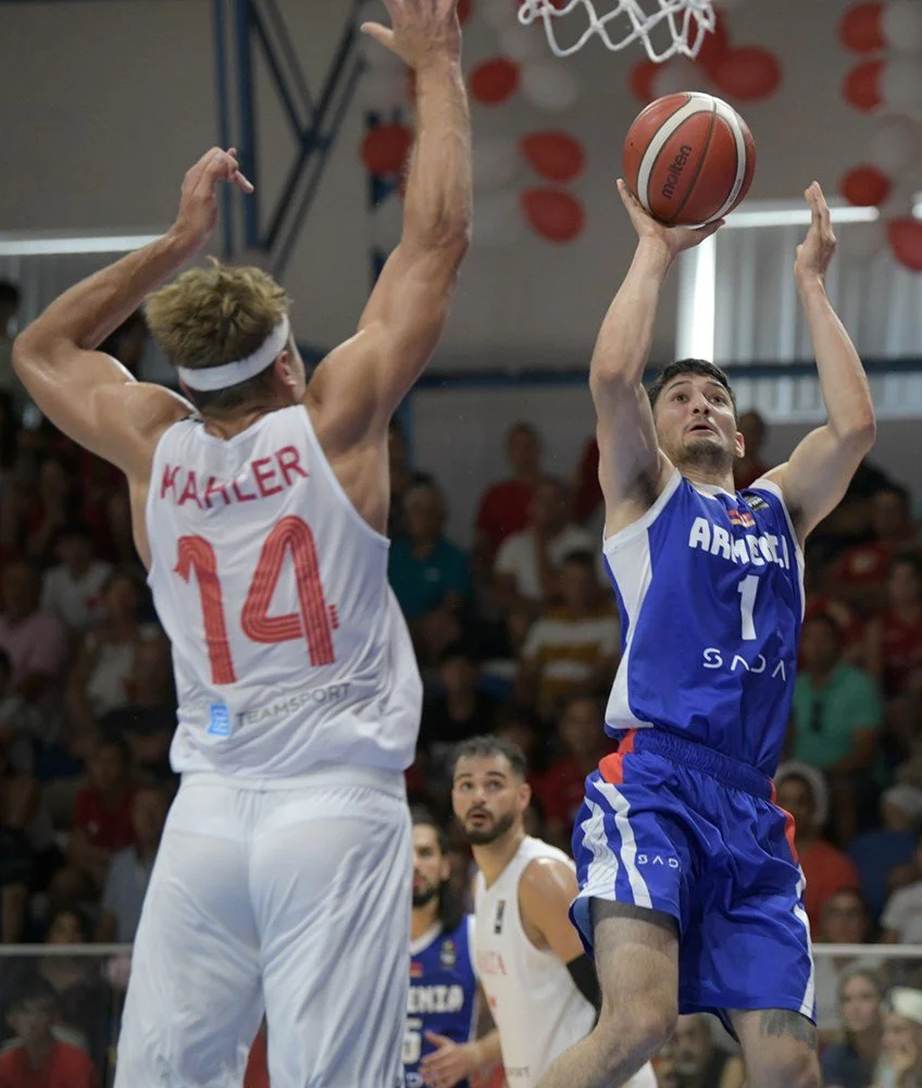 Basketball game with player in blue jersey shooting over player in white jersey