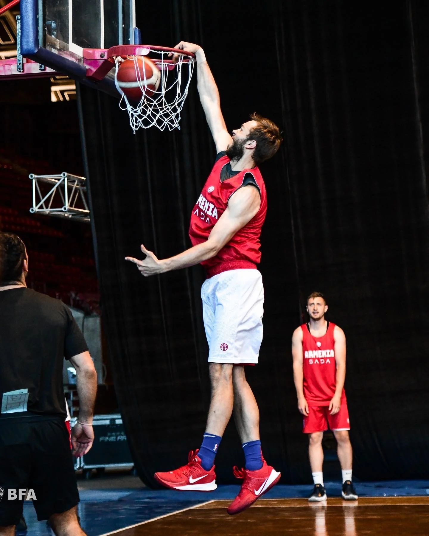 Basketball player dunking during practice with teammates watching.
