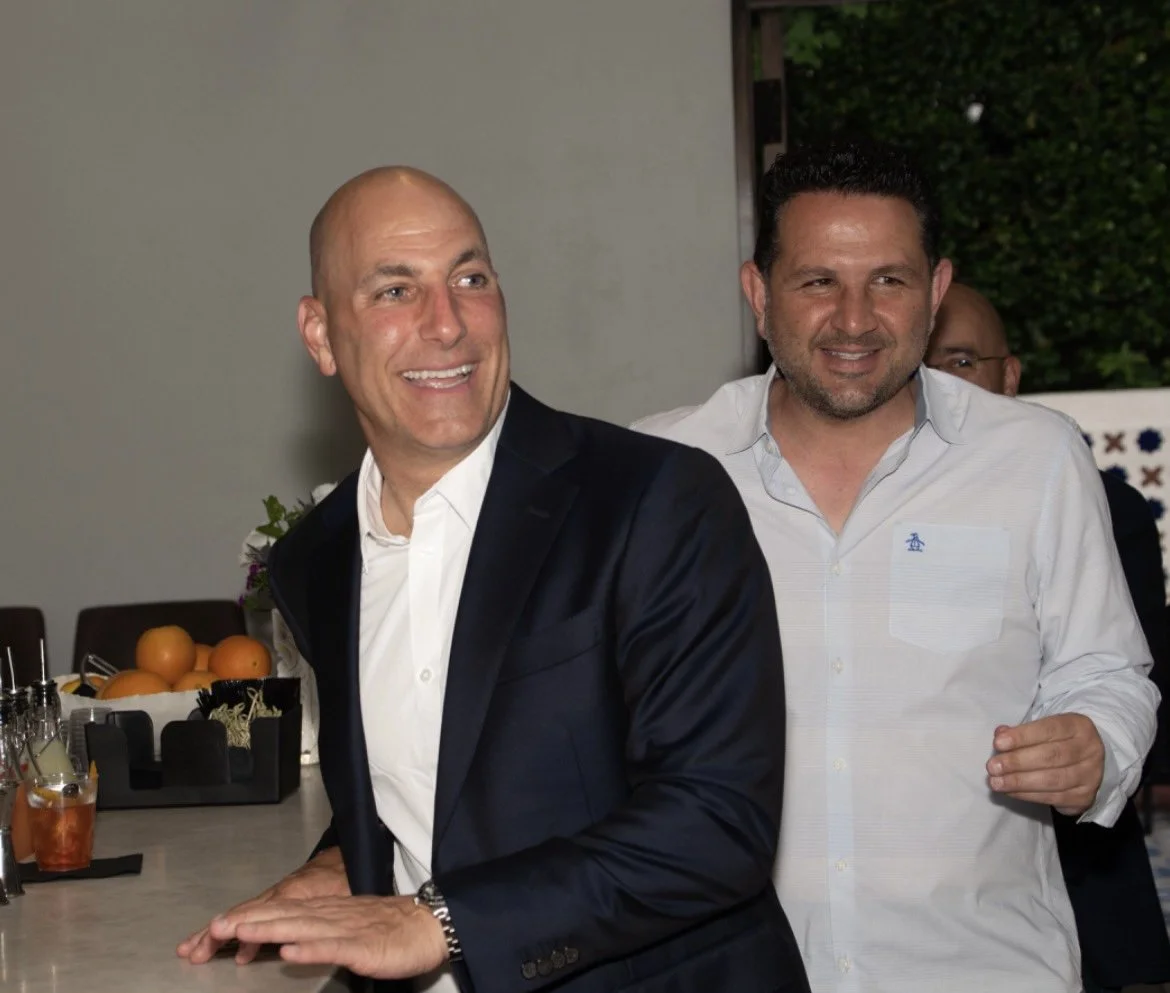 Two men standing at a table with drinks and fruits