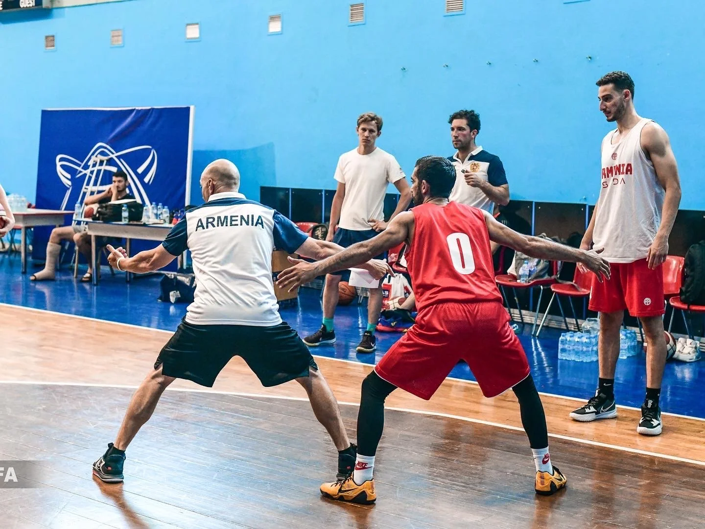 Basketball training session with players and coaches on an indoor court, featuring practice drills and discussions.