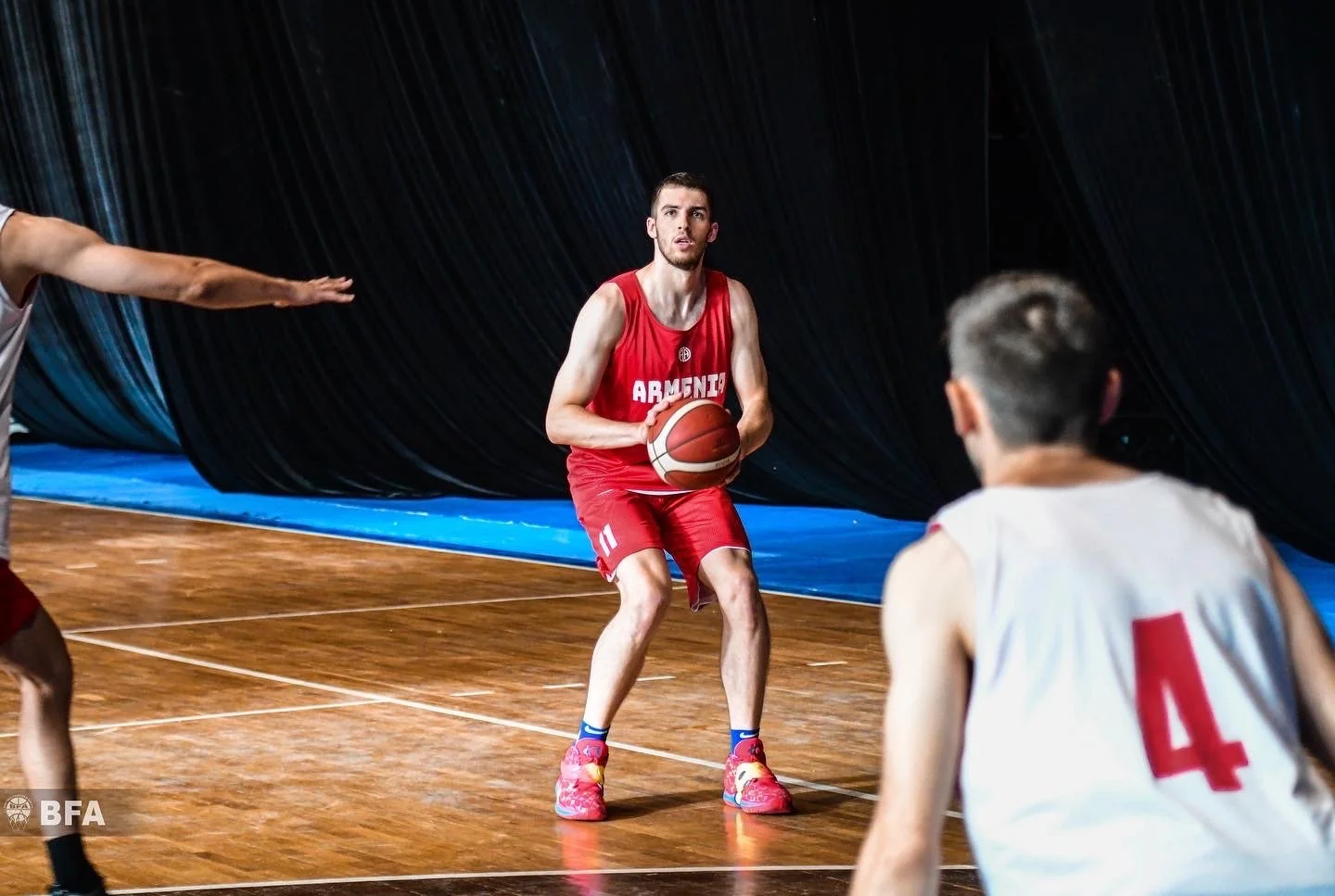 Basketball player in red jersey prepares to pass ball on indoor court during game with teammates.