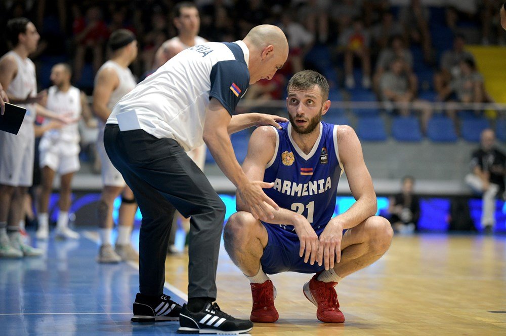 Basketball coach talking to a player wearing an Armenia jersey during a game.
