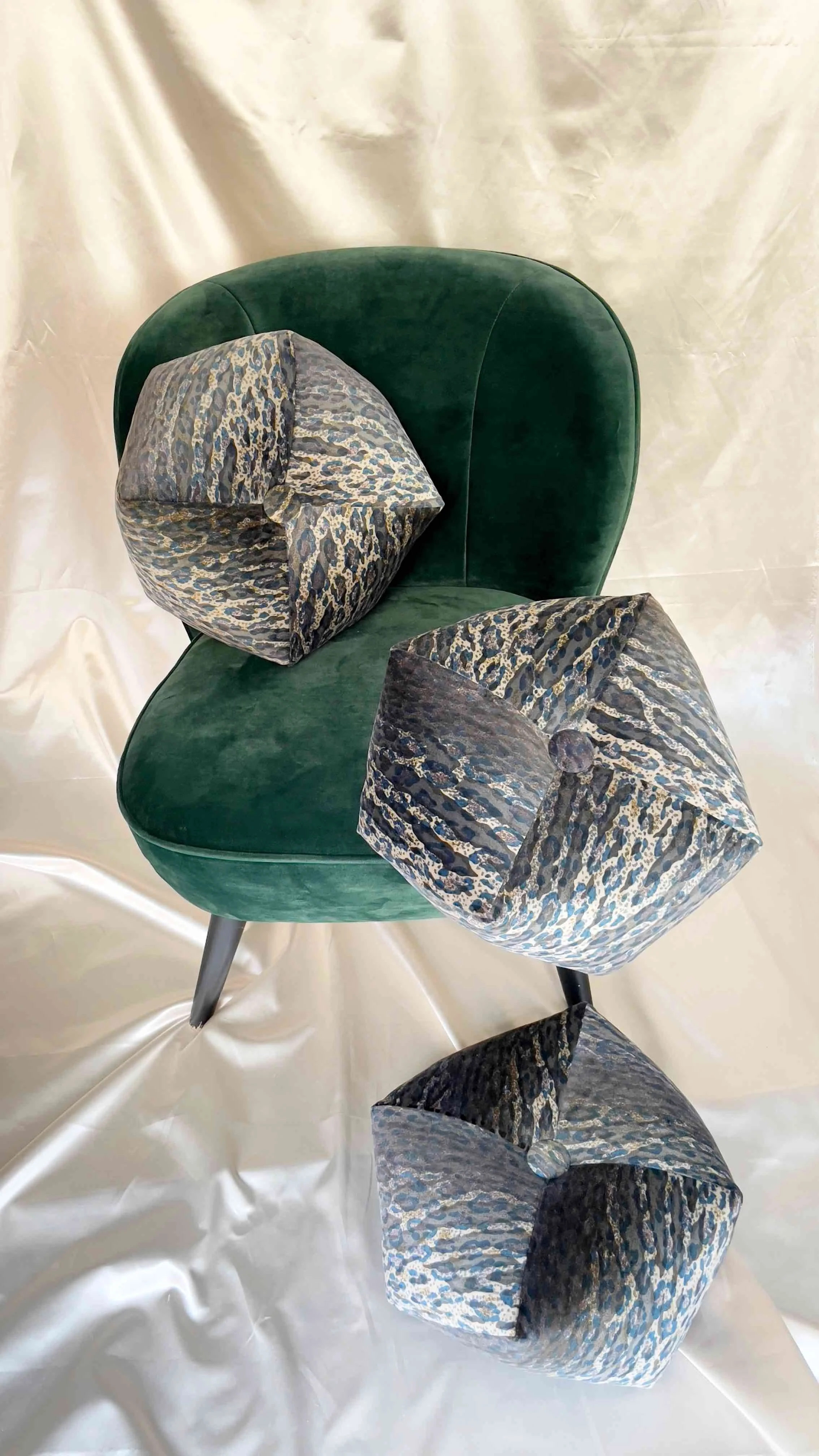 Three octagon pillows with blue pattern on green velvet chair.