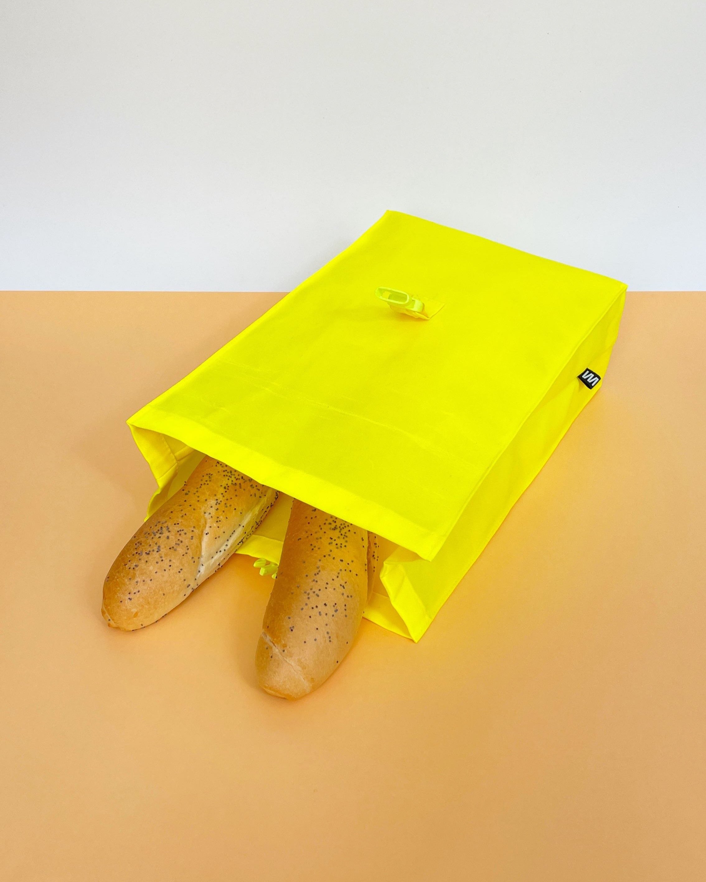 Neon yellow beeswax bag lying flat with the top open, containing two poppy seed bread rolls.