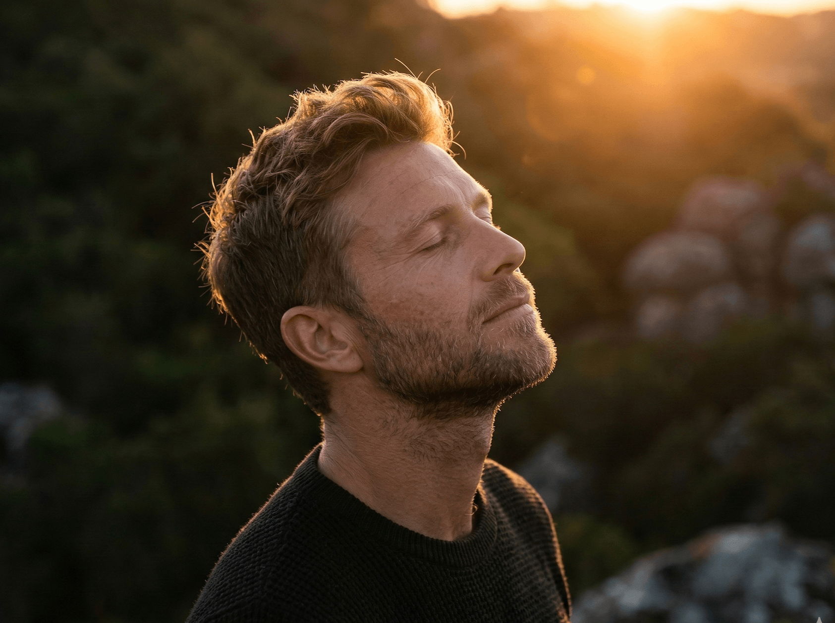 Ein Mann mit closed eyes, der bei Sonnenuntergang entspannt aussieht, im Freien, umgeben von Natur. Empfindet Ruhe.