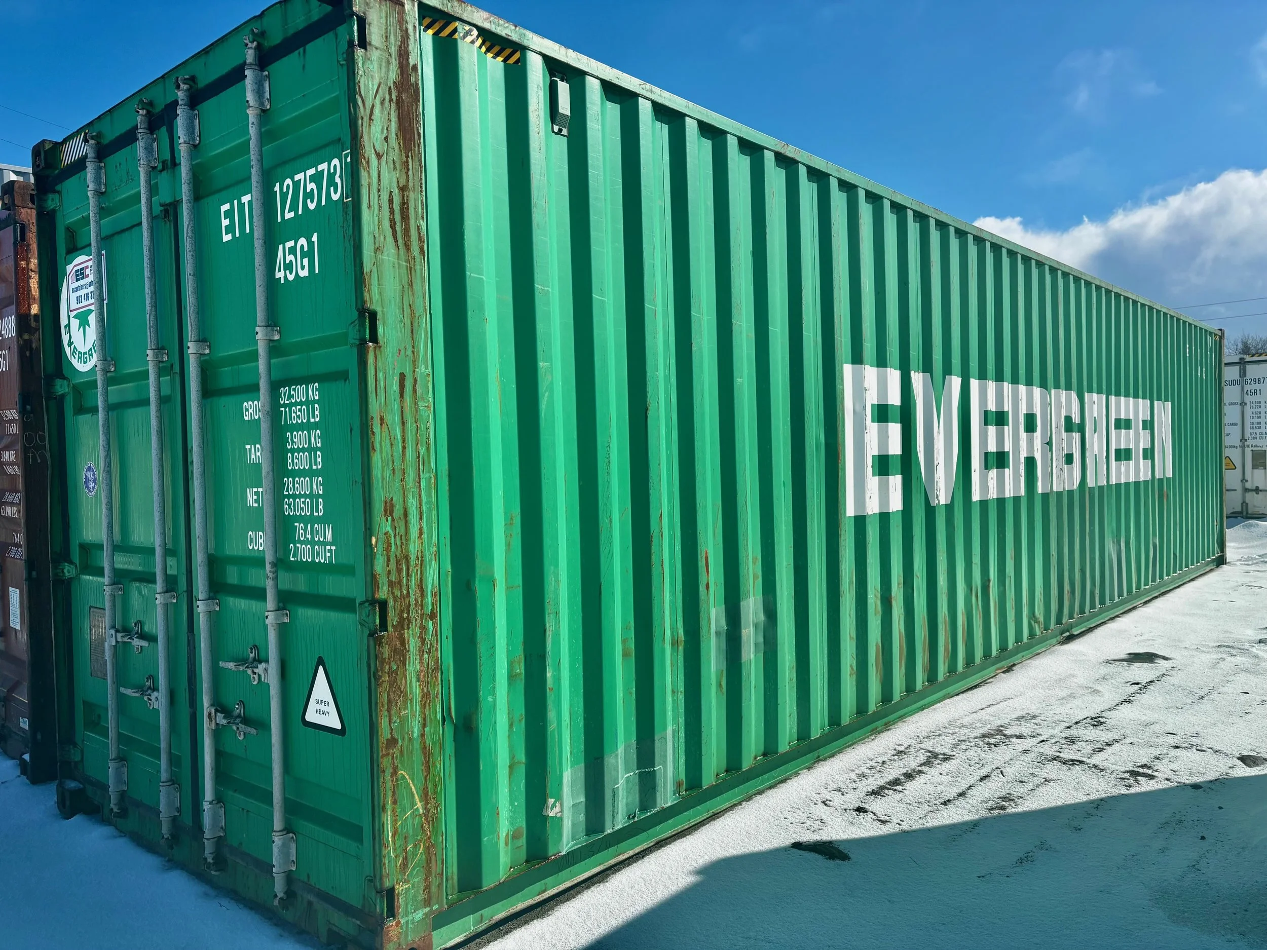 Green shipping container with the logo EVR GREEN on the side, standing on snow under a blue sky.