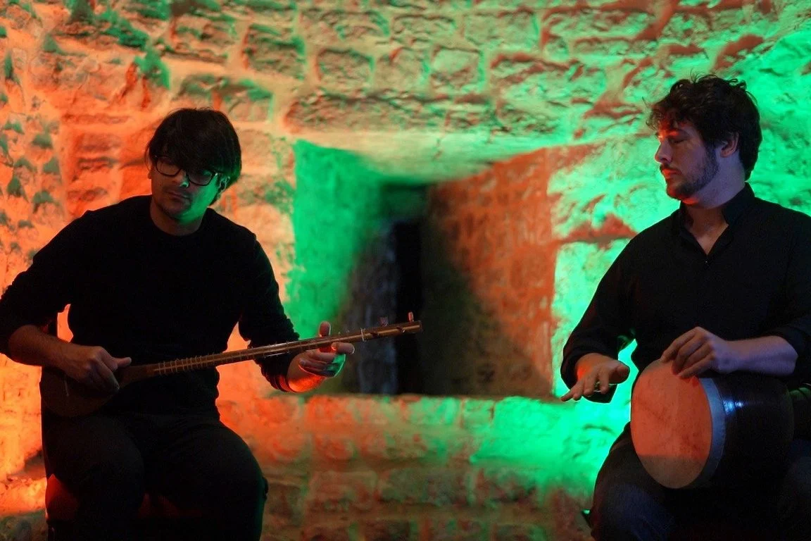 Deux musiciens dans un environnement à éclairage coloré jouent du tambour et du luth.