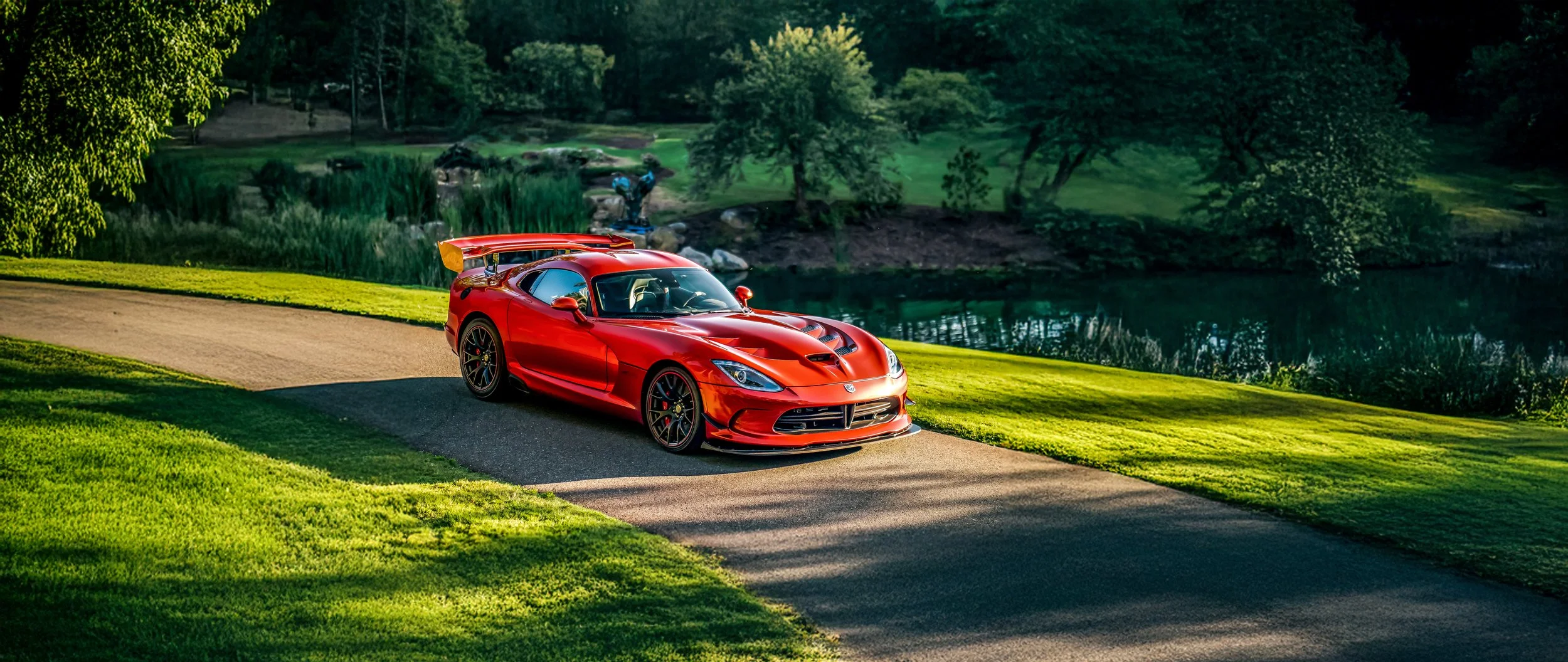 Red sports car on a driveway beside a lake with green trees and grass in the background.