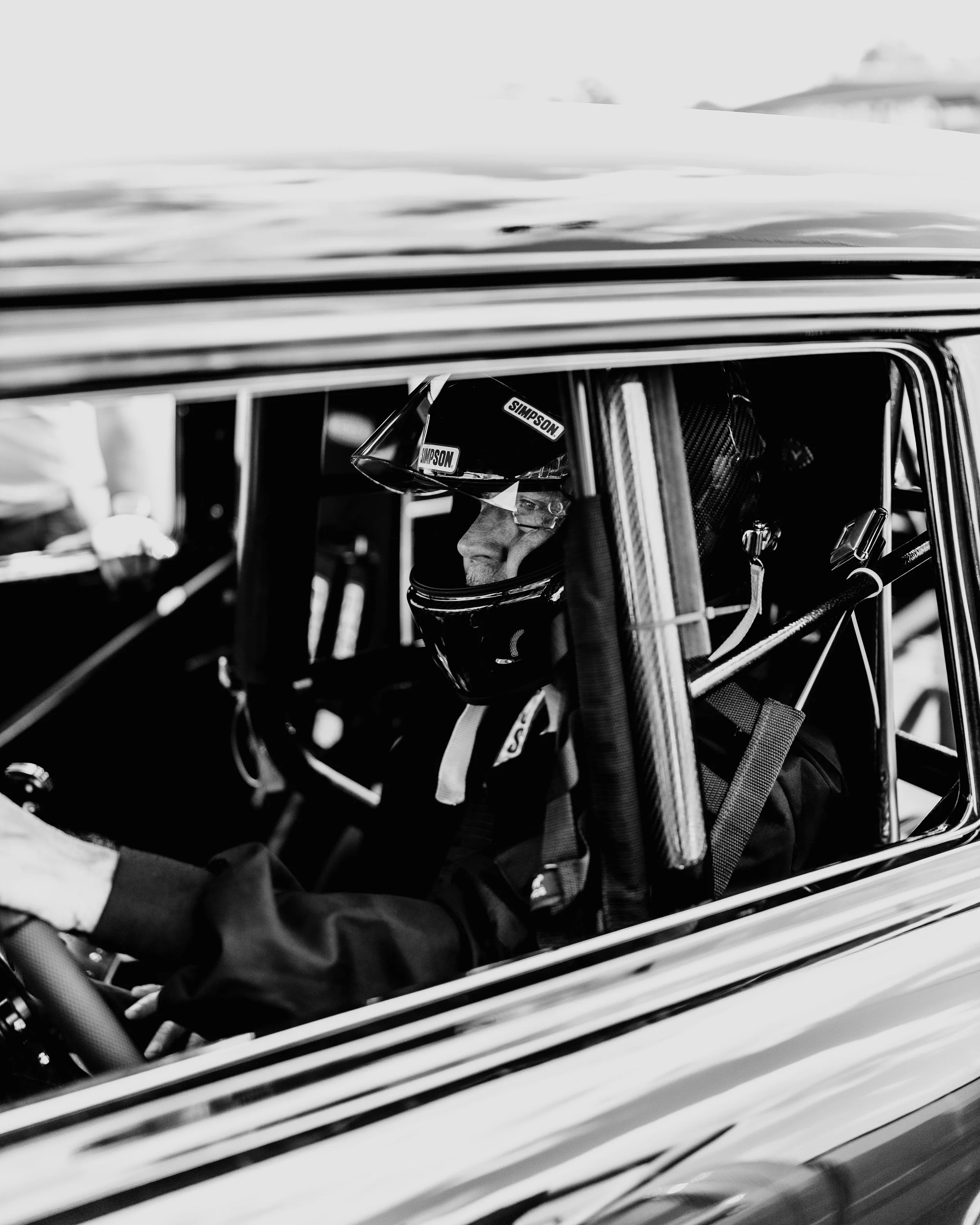 A race car driver wearing a helmet and racing suit sitting inside a racing vehicle.