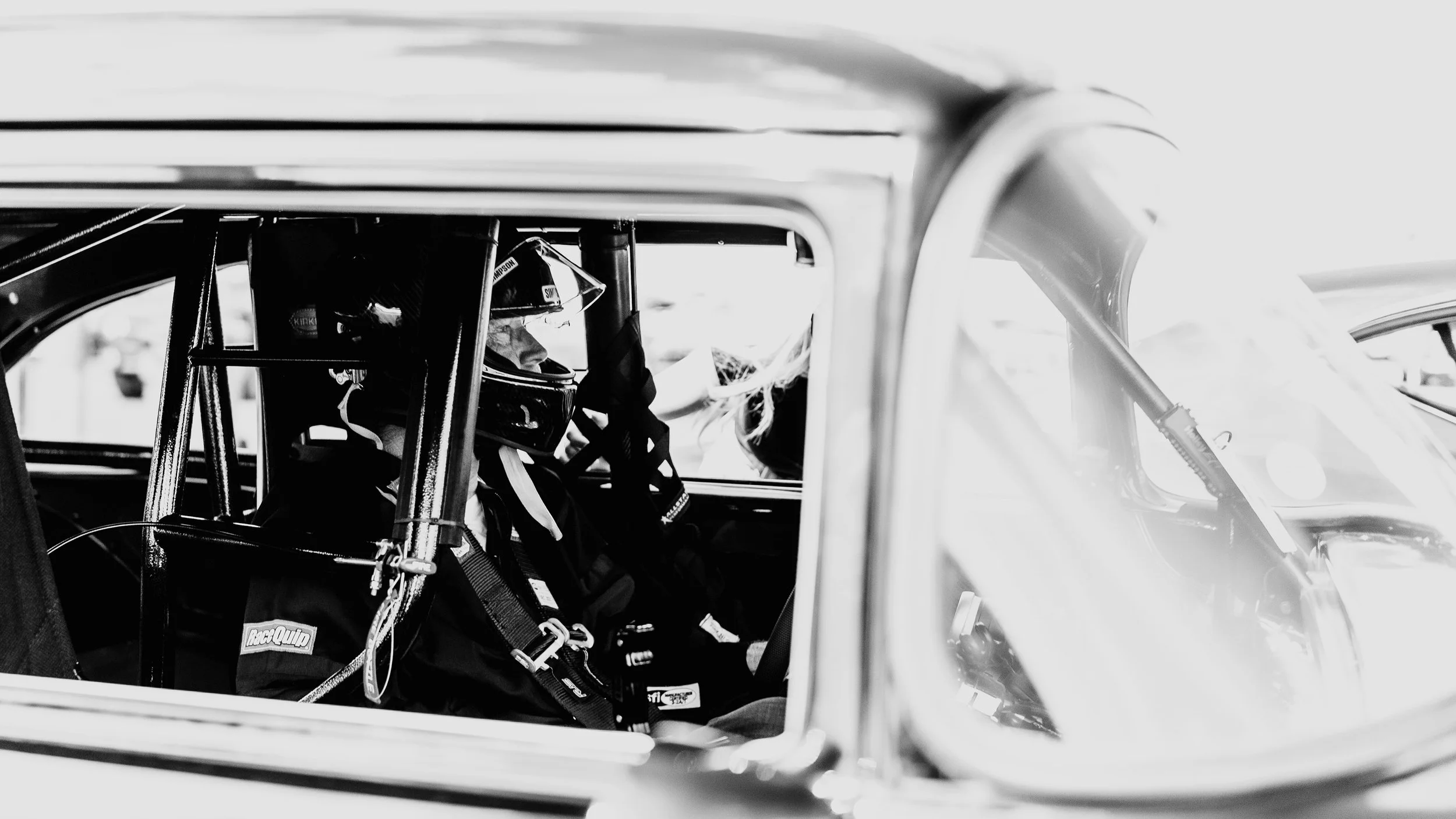 A racing driver inside a race car, wearing a helmet and racing suit, preparing for a race.