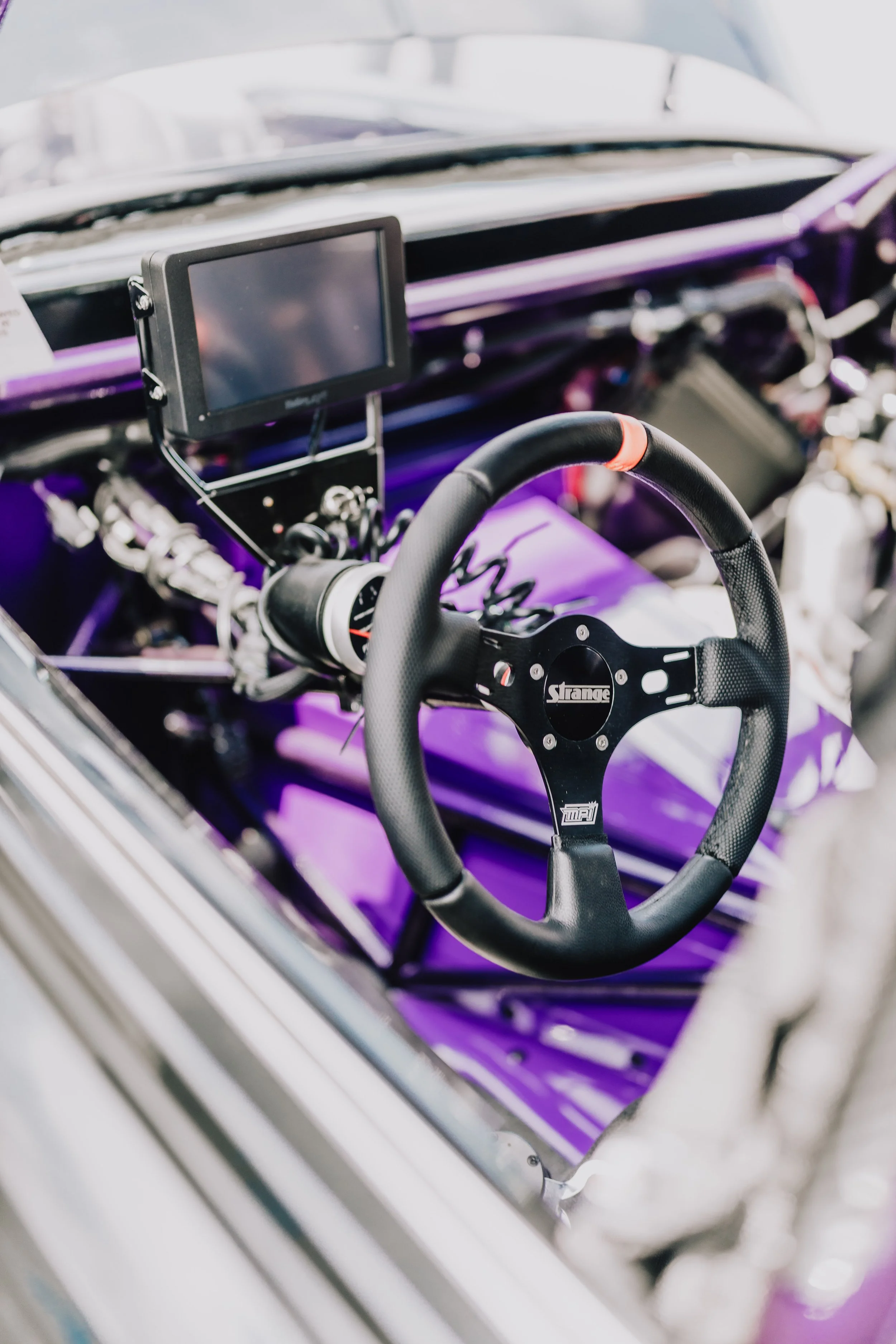 Interior of a race car with a steering wheel, digital display, and purple dashboard.
