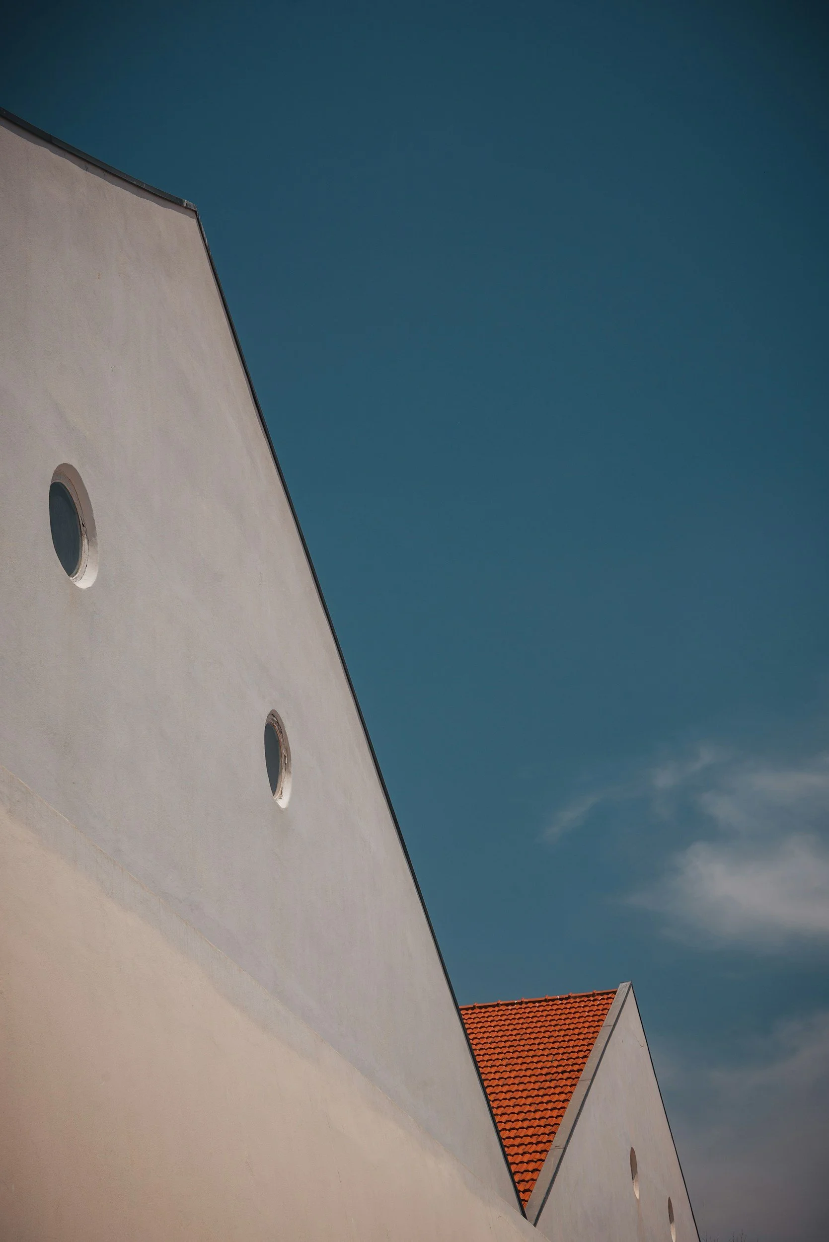 Una veduta di un edificio bianco con quattro finestre rotonde e un tetto rosso, contro un cielo azzurro con alcune nuvole.