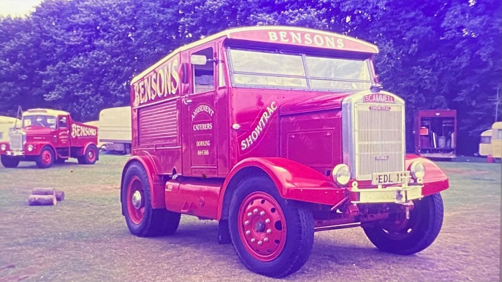 Vintage red truck with "Benson's" logo parked on grass, lined by trees.