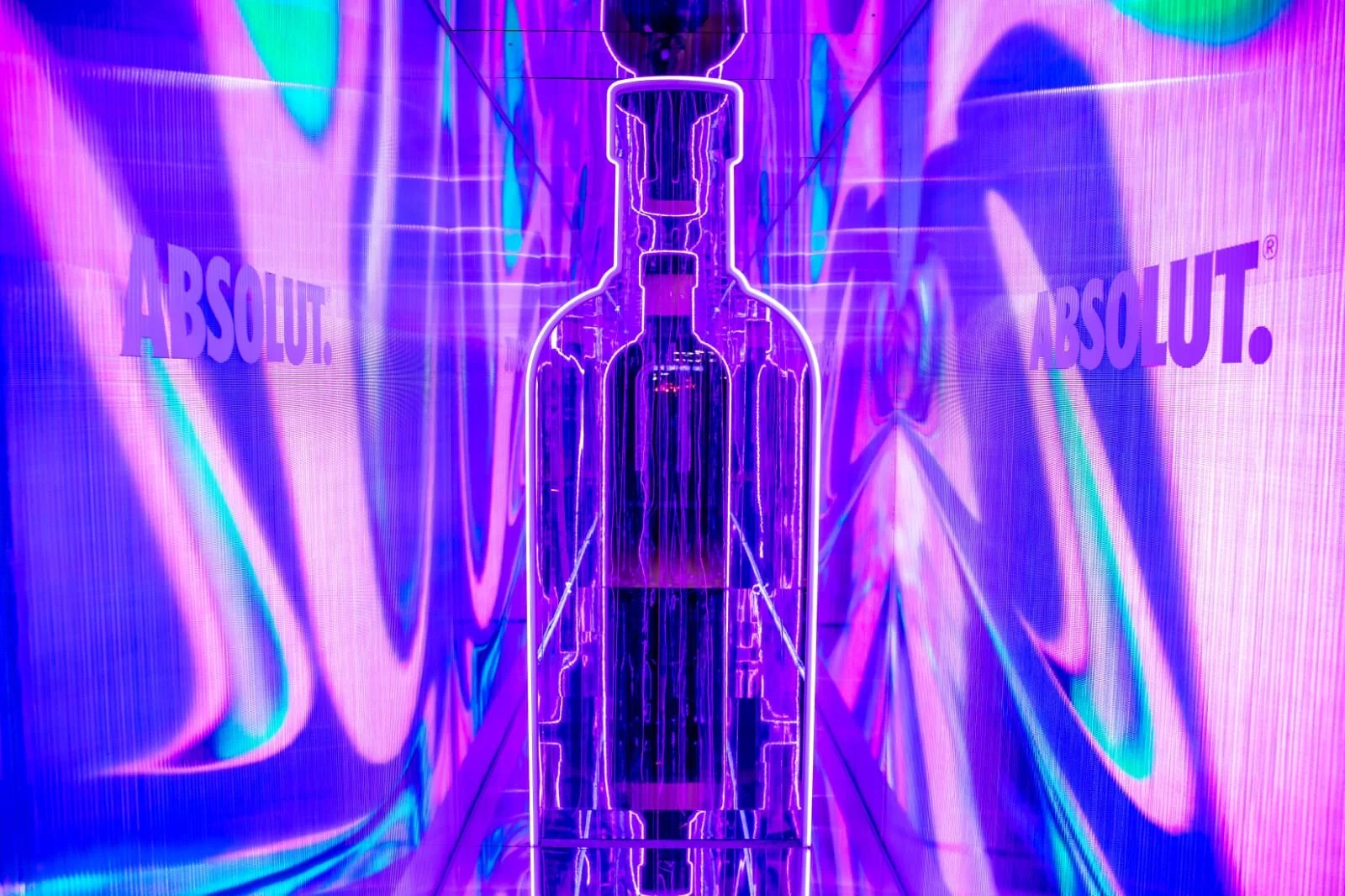 A neon art installation of a bottle with purple, blue, and pink lighting, featuring the word 'ABSOLUT.' on the background walls.