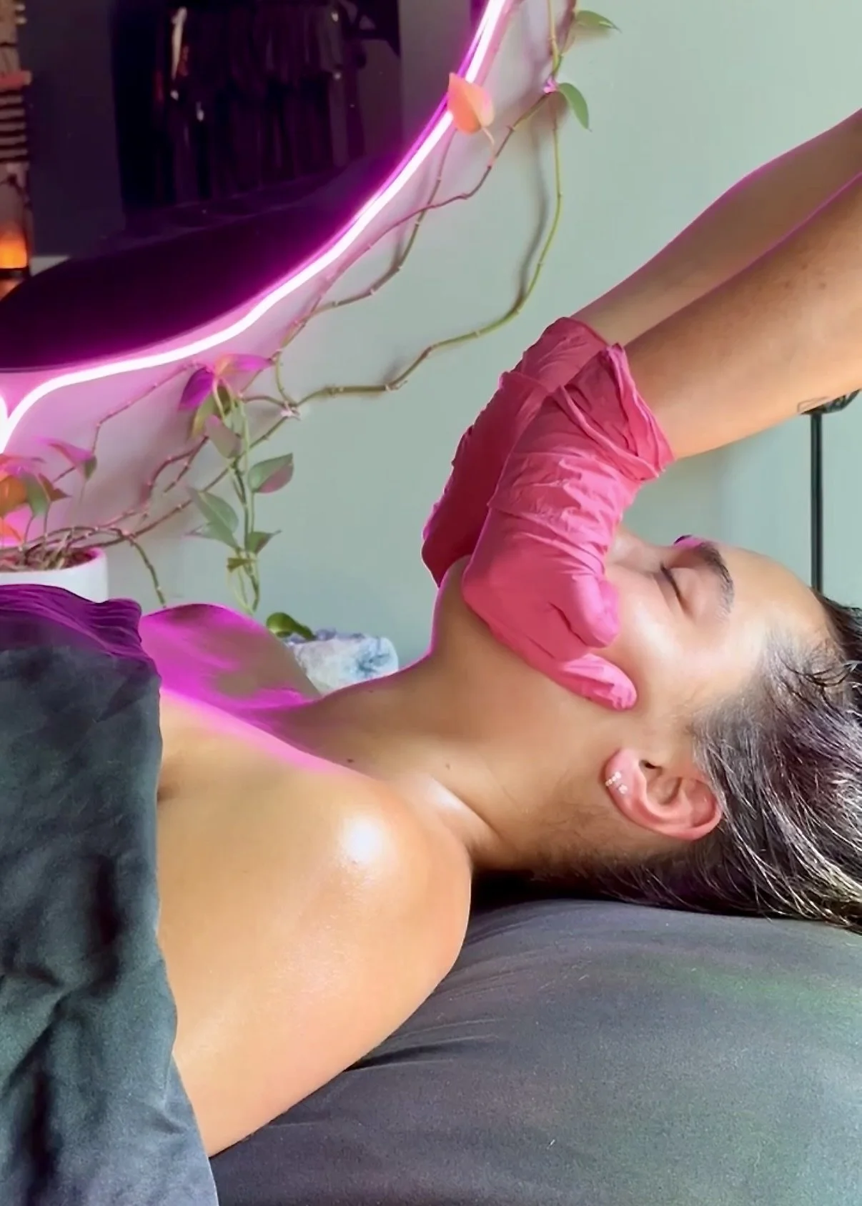 Client rests on a treatment table while an esthetician performs buccal massage around the mouth, cheek, and jaw during a facial at Bath House.