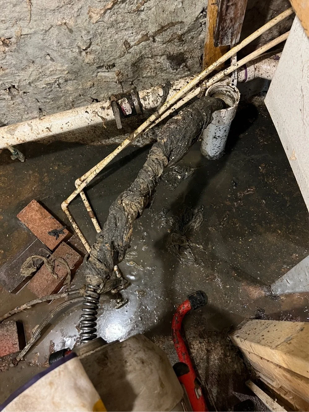 A wet, dirty plumbing area with pipes, a valve, and a water leak on the floor.