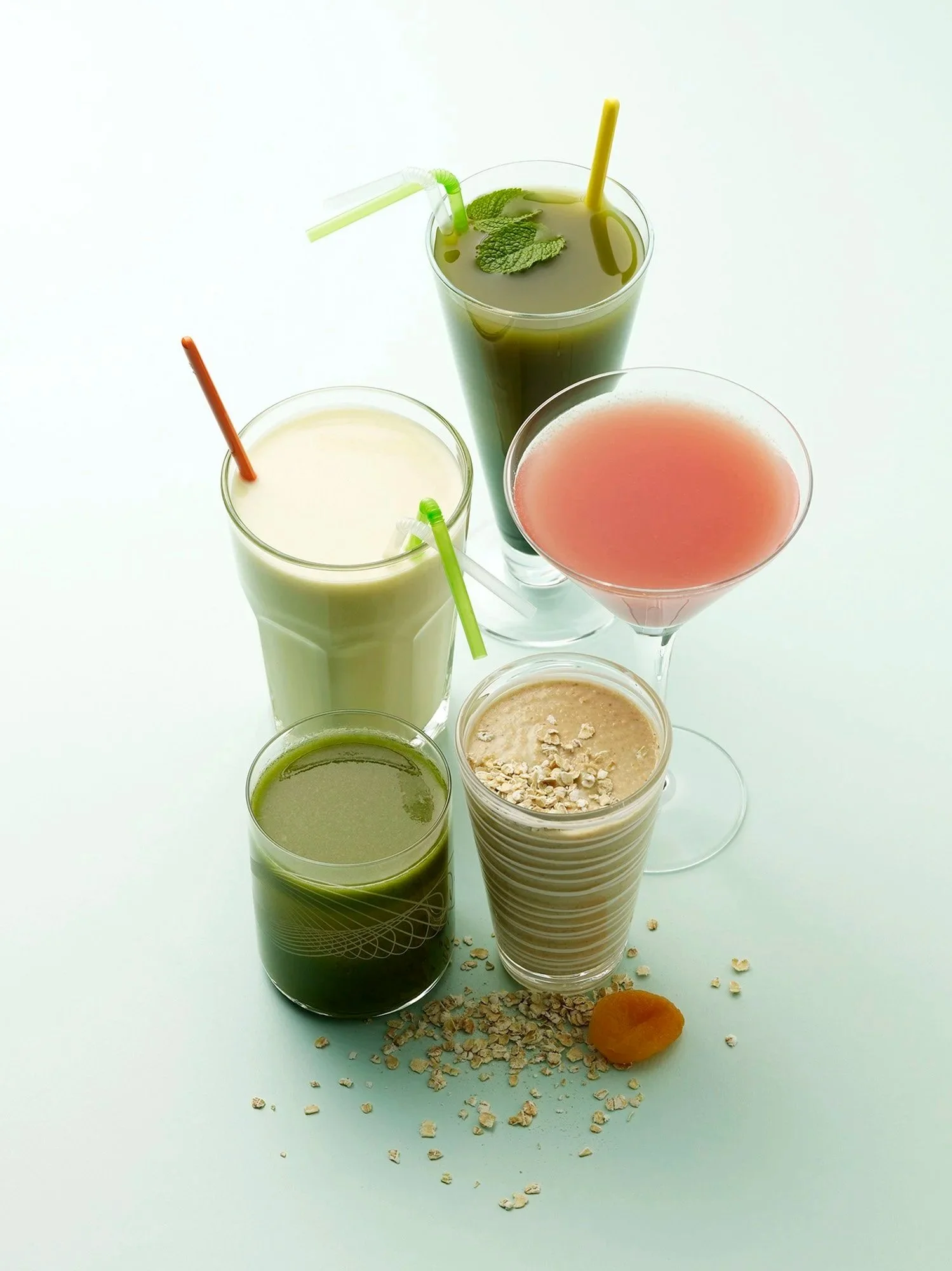 A variety of healthy beverages including green detox juices, protein smoothies with rolled oats, and antioxidant-rich fruit blends and a creamy oat-topped smoothie.