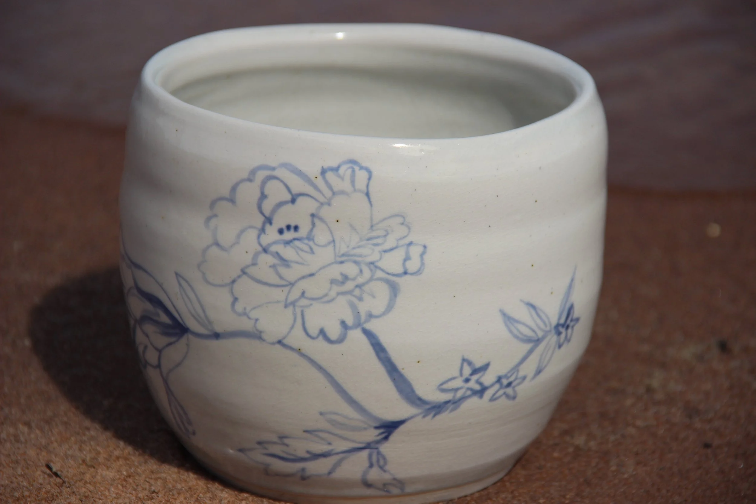 A white ceramic cup with blue floral design resting on a brown surface.