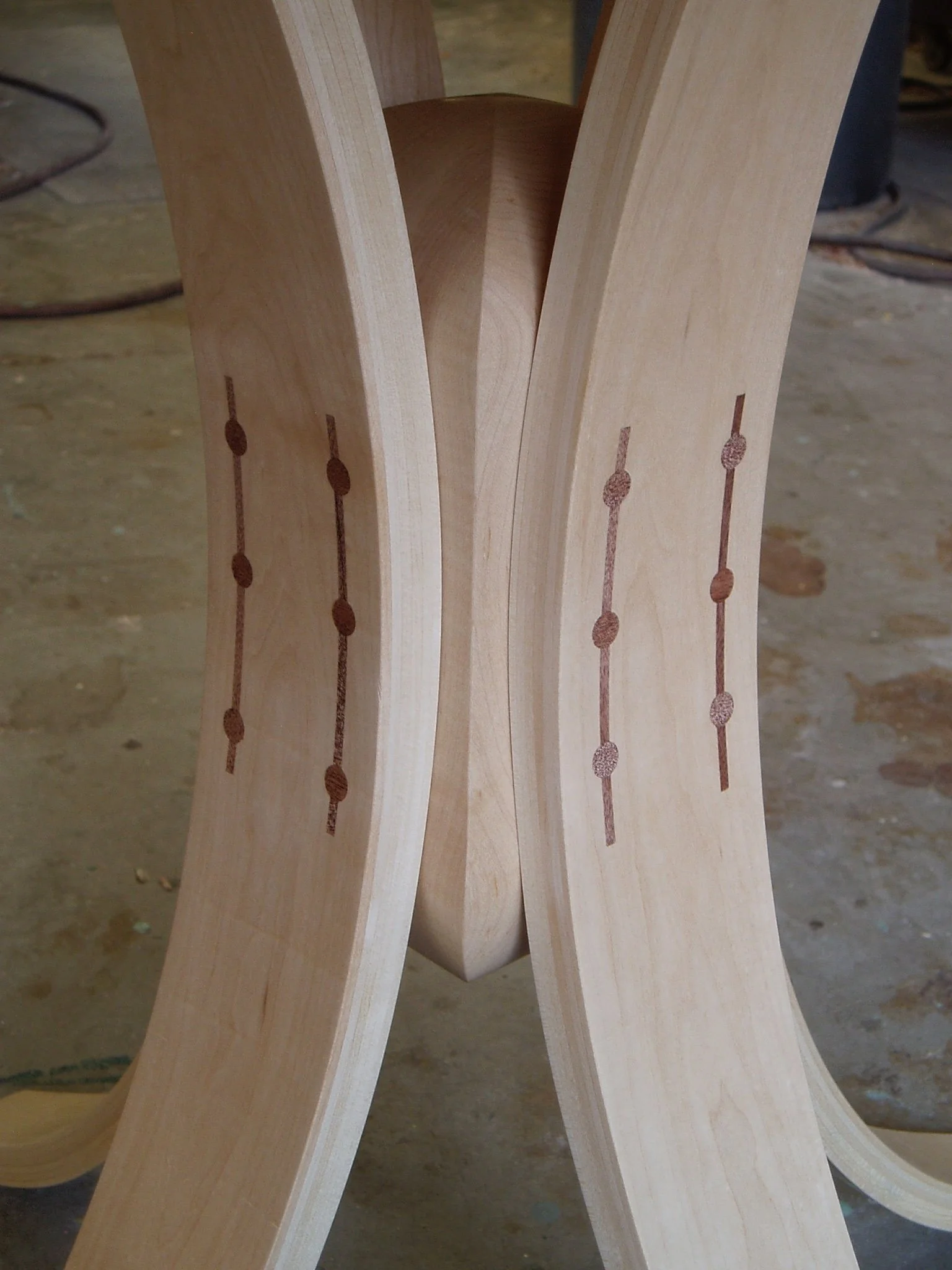 A close view of a table pedestal. Swoop in towards the center and back out as they reach the floor. Parallel lines bisect columns of dots in a decorative pattern where the legs join in the middle.