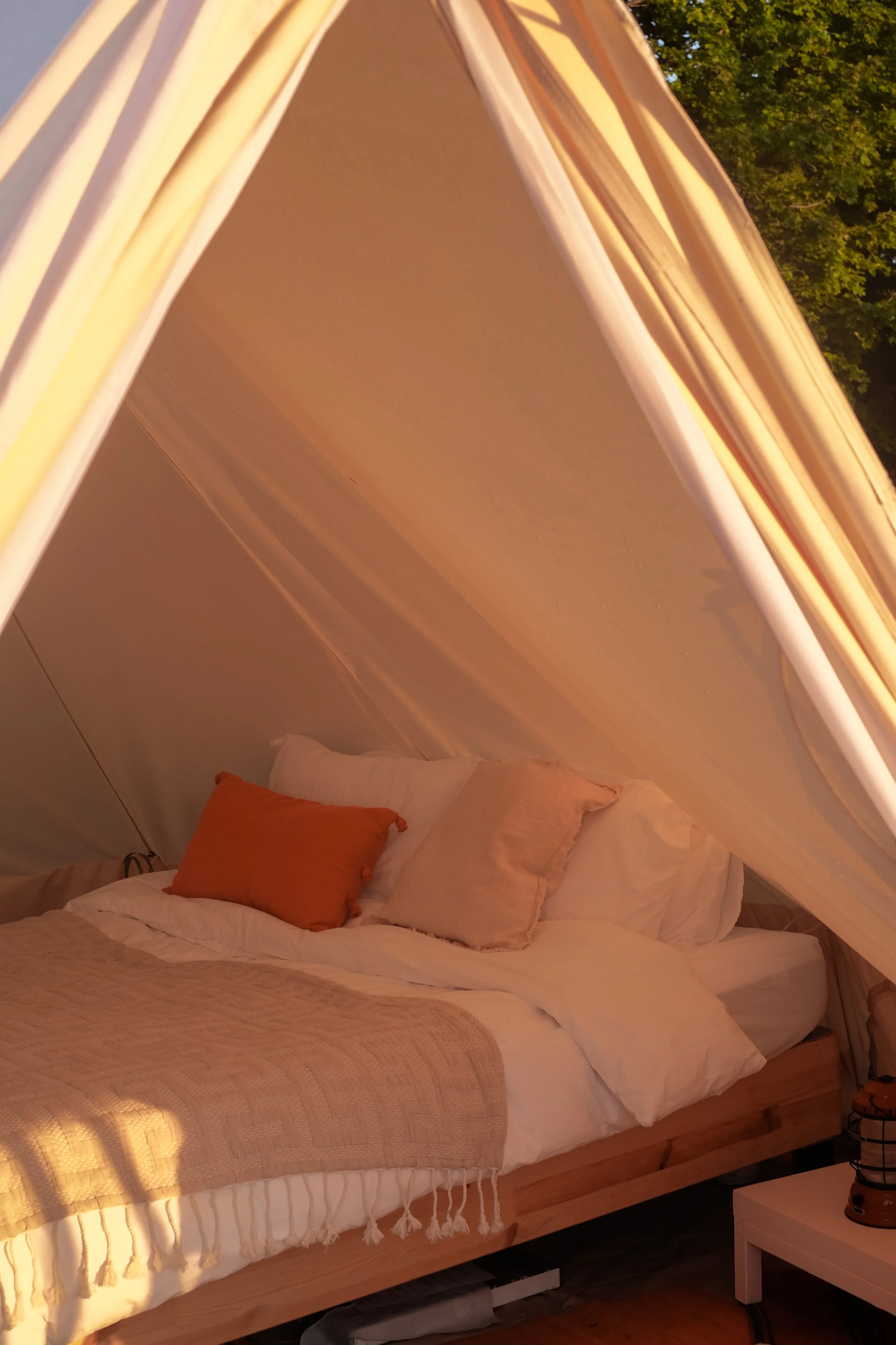glamping tent interior with soft neutrals, a queen size bed with white linens int he frame of the glamping tent