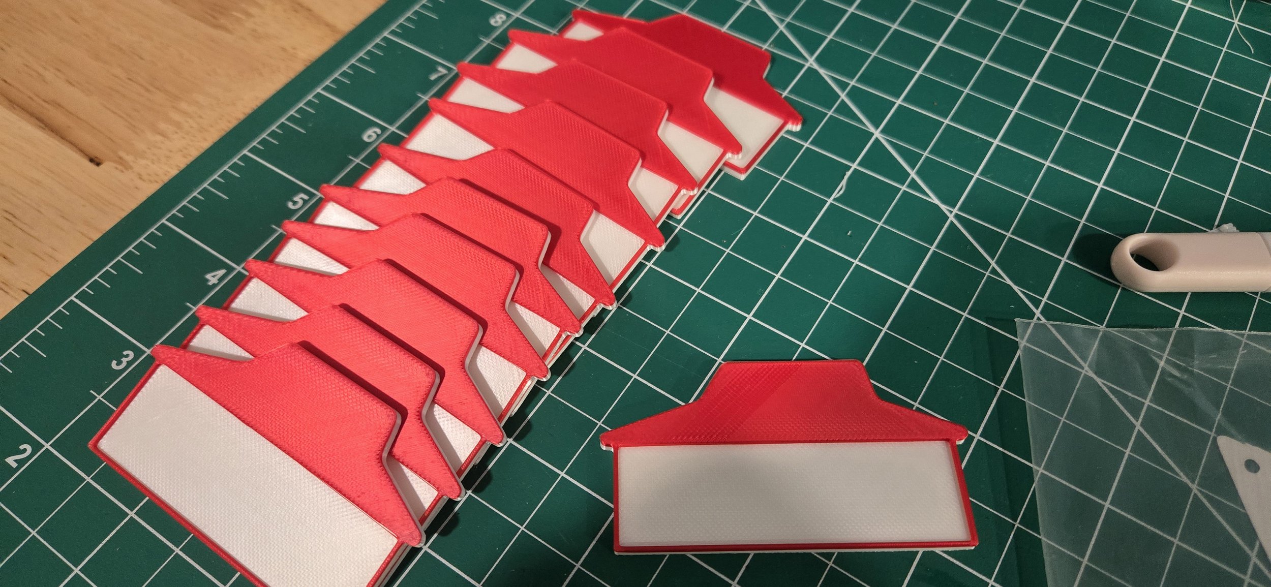 Multiple red and white house-shaped labels arranged on a green cutting mat, with some supplies visible nearby.