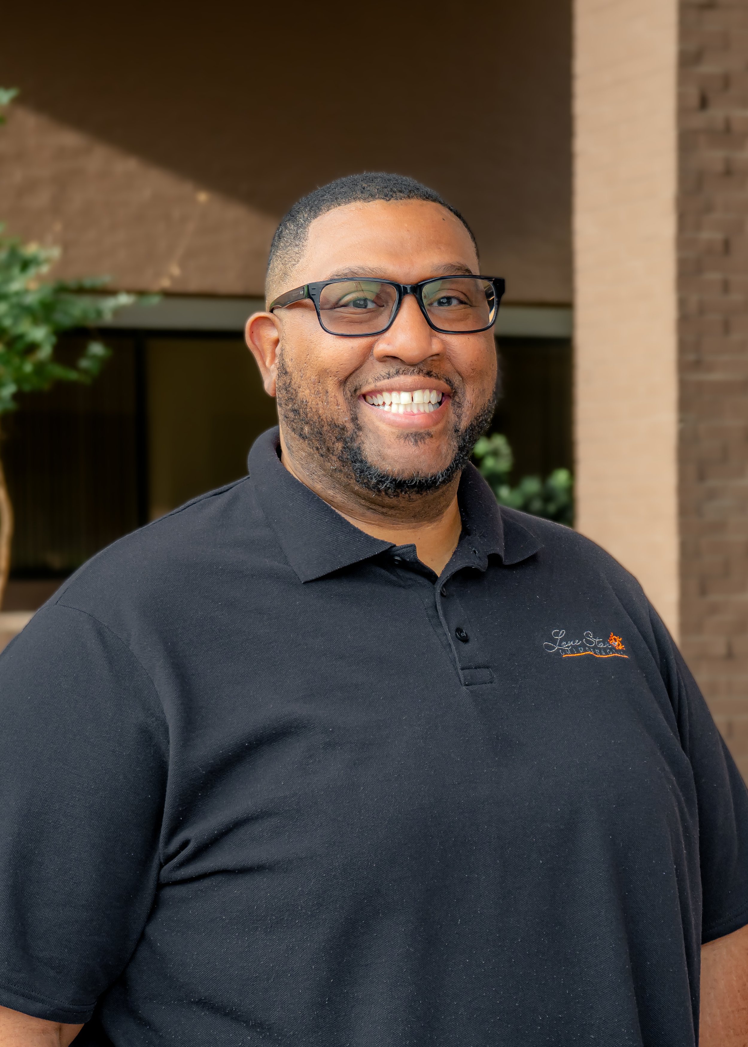 Smiling person wearing glasses and a black polo shirt outdoors