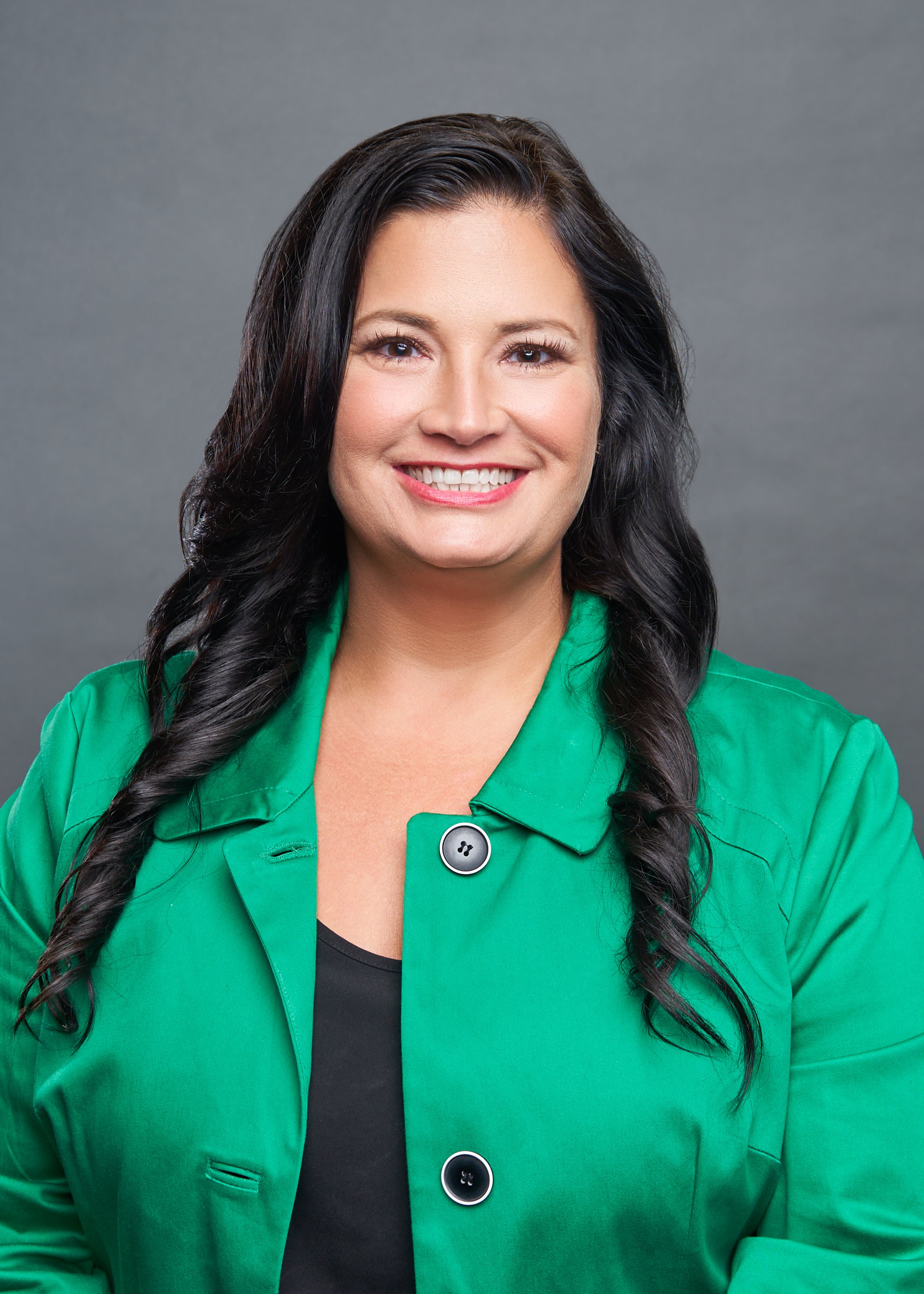 Woman smiling in a green coat against a gray background. Hempstead Staff Headshots.