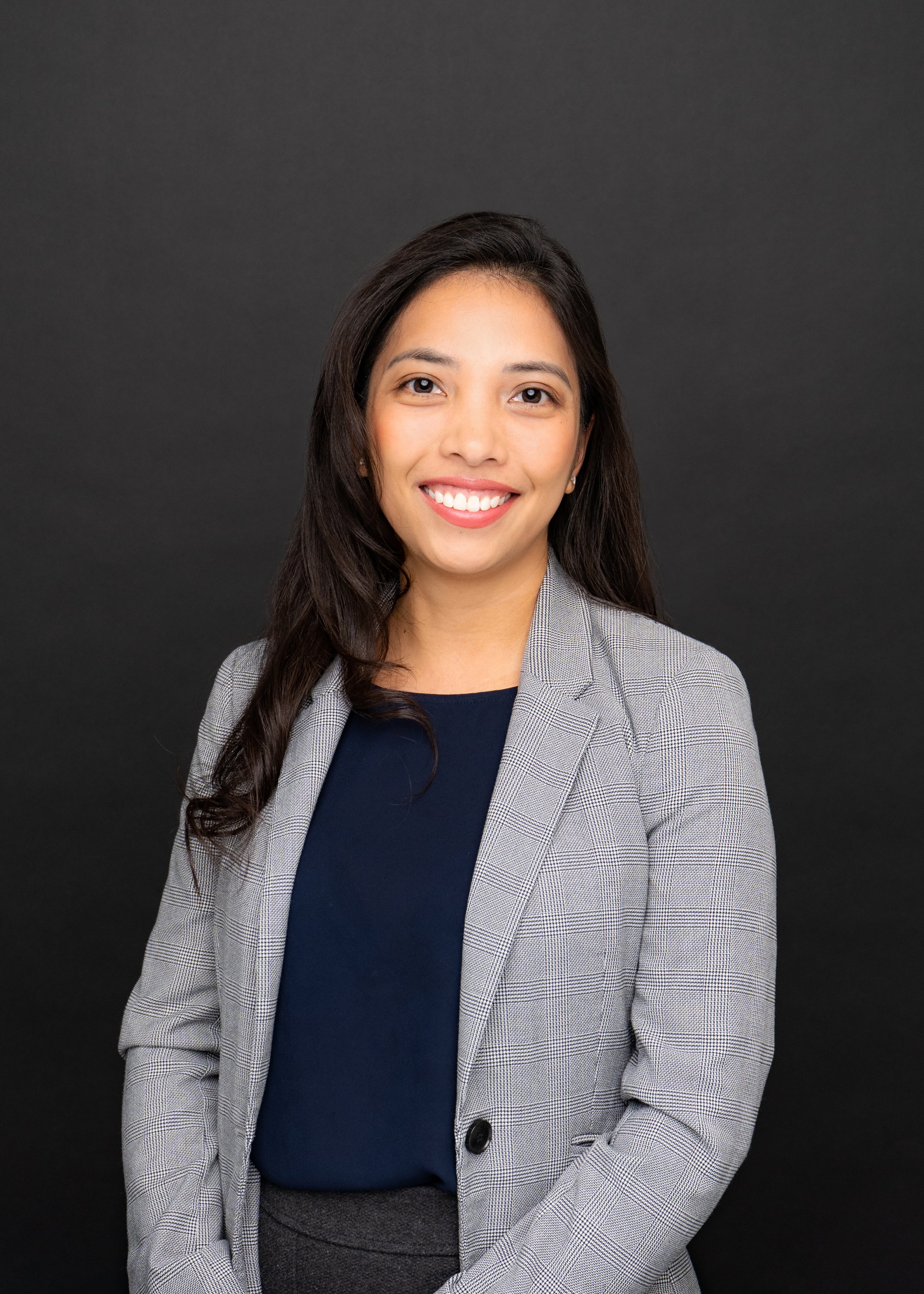 Professional woman in a blazer smiling against a black background. Clutch City Insurance Staff Headshot.