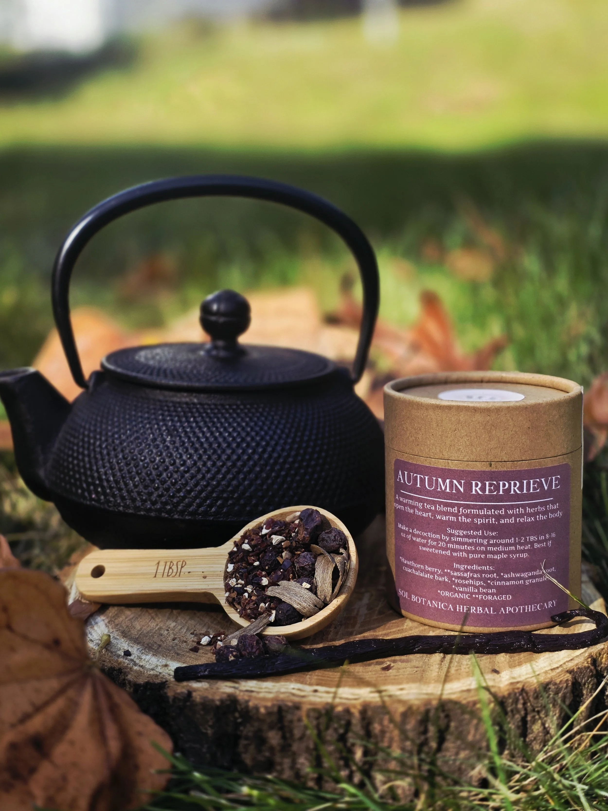 black iron teapot, rose colored container of tea, wooden scoop full of looseleaf tea