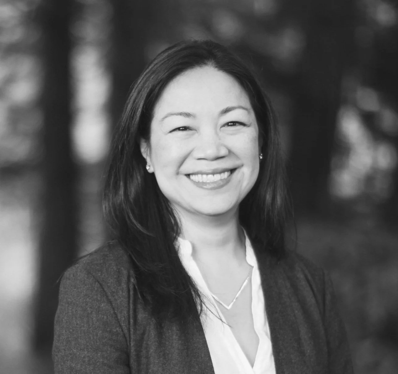 Smiling person in black and white portrait with blurred outdoor background.