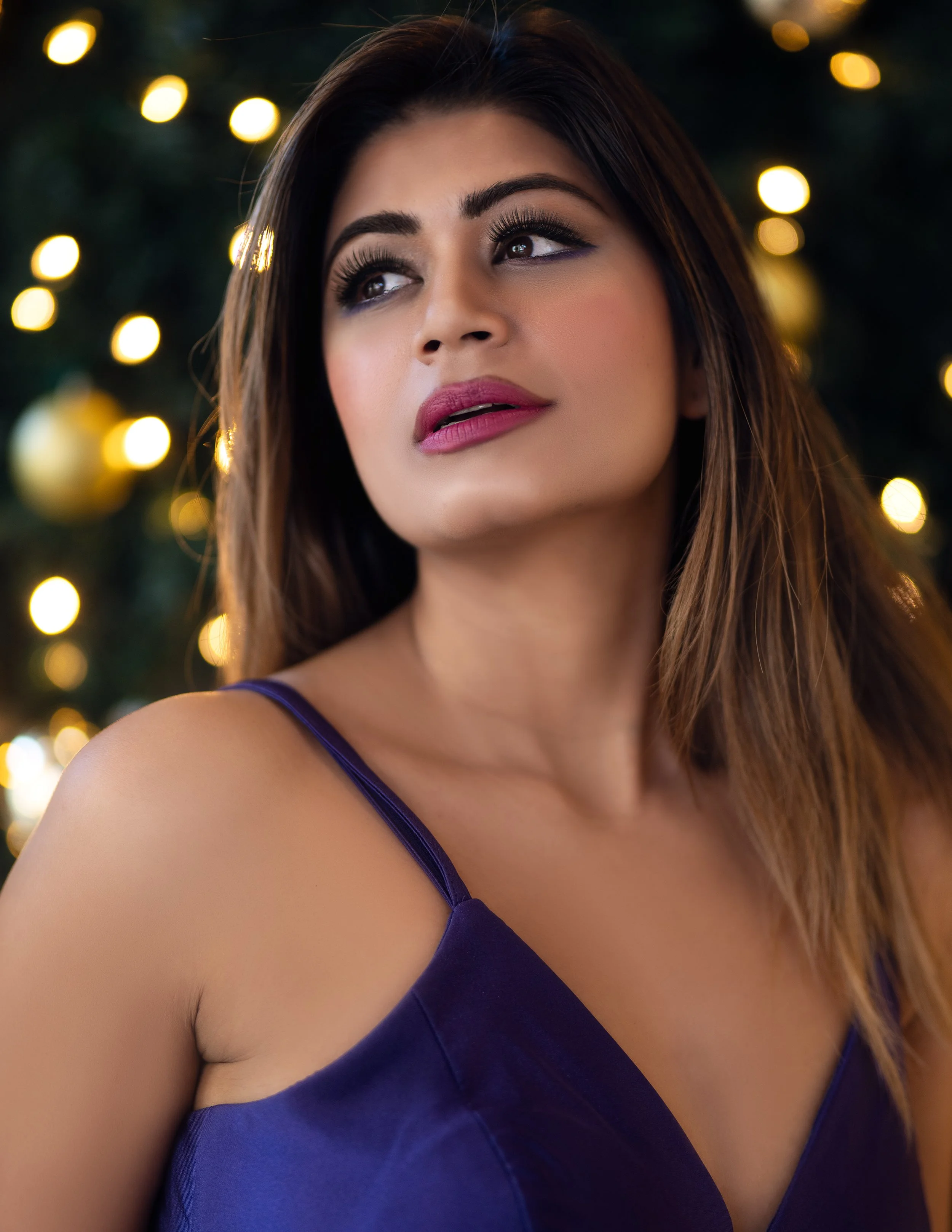 Editorial close-up portrait of Yesmin in a purple dress with warm bokeh lights in the background