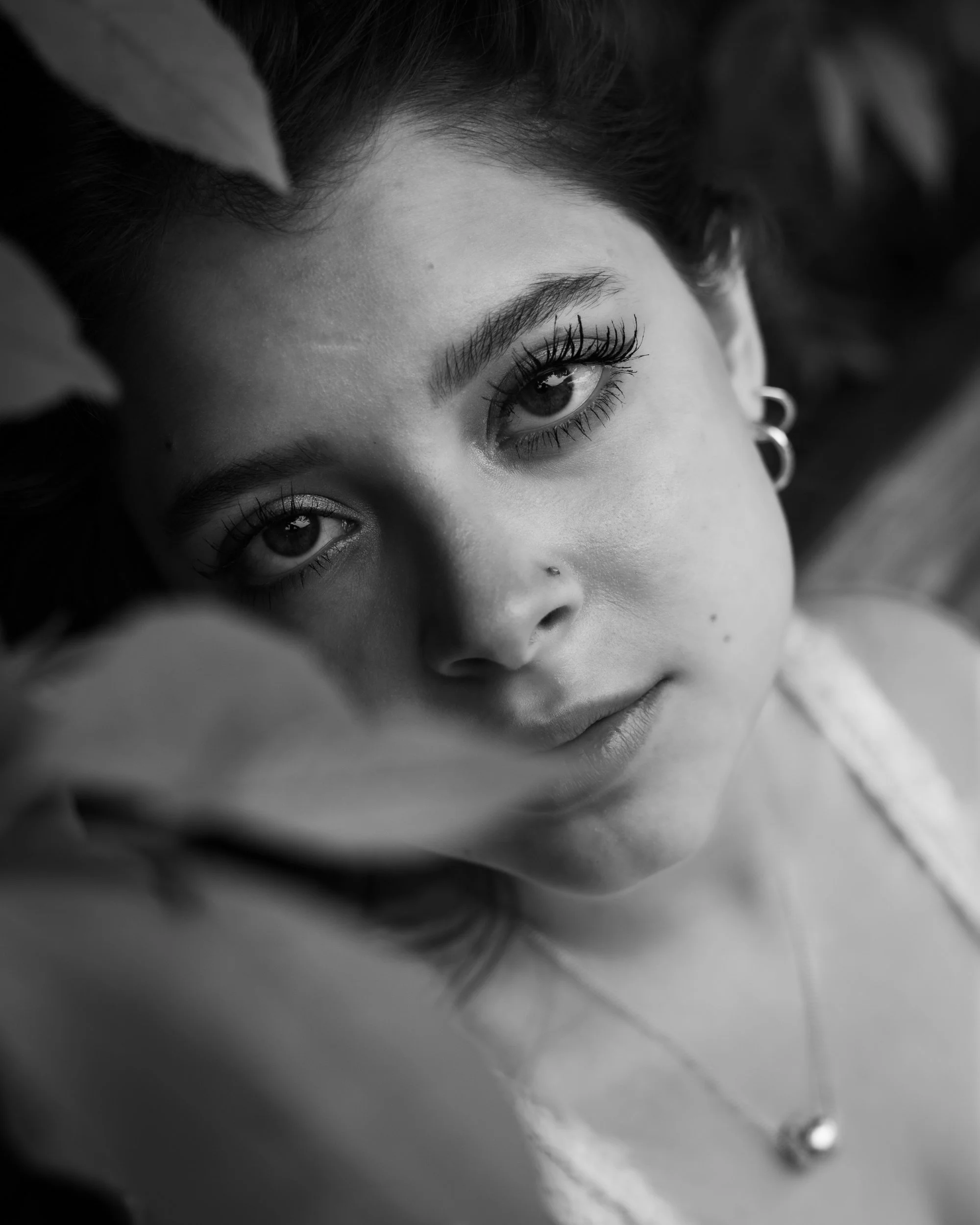 Black and white editorial close-up portrait of Julianna framed by leaves with soft natural light