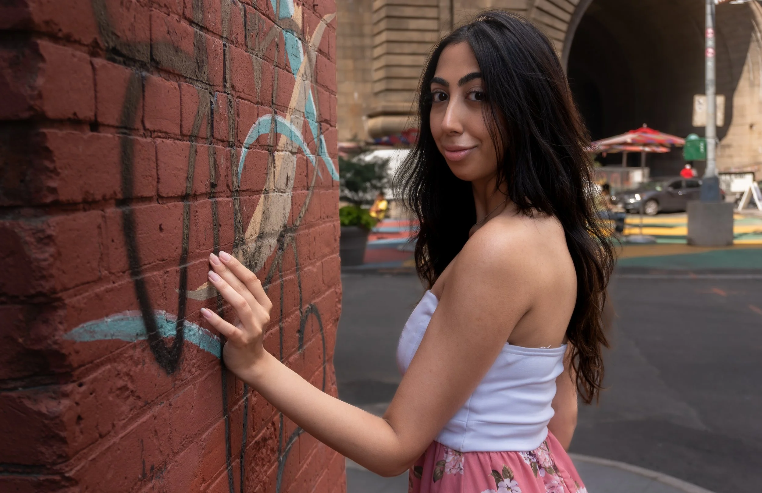 Editorial portrait of Harshita standing by a graffiti brick wall in an urban New York setting