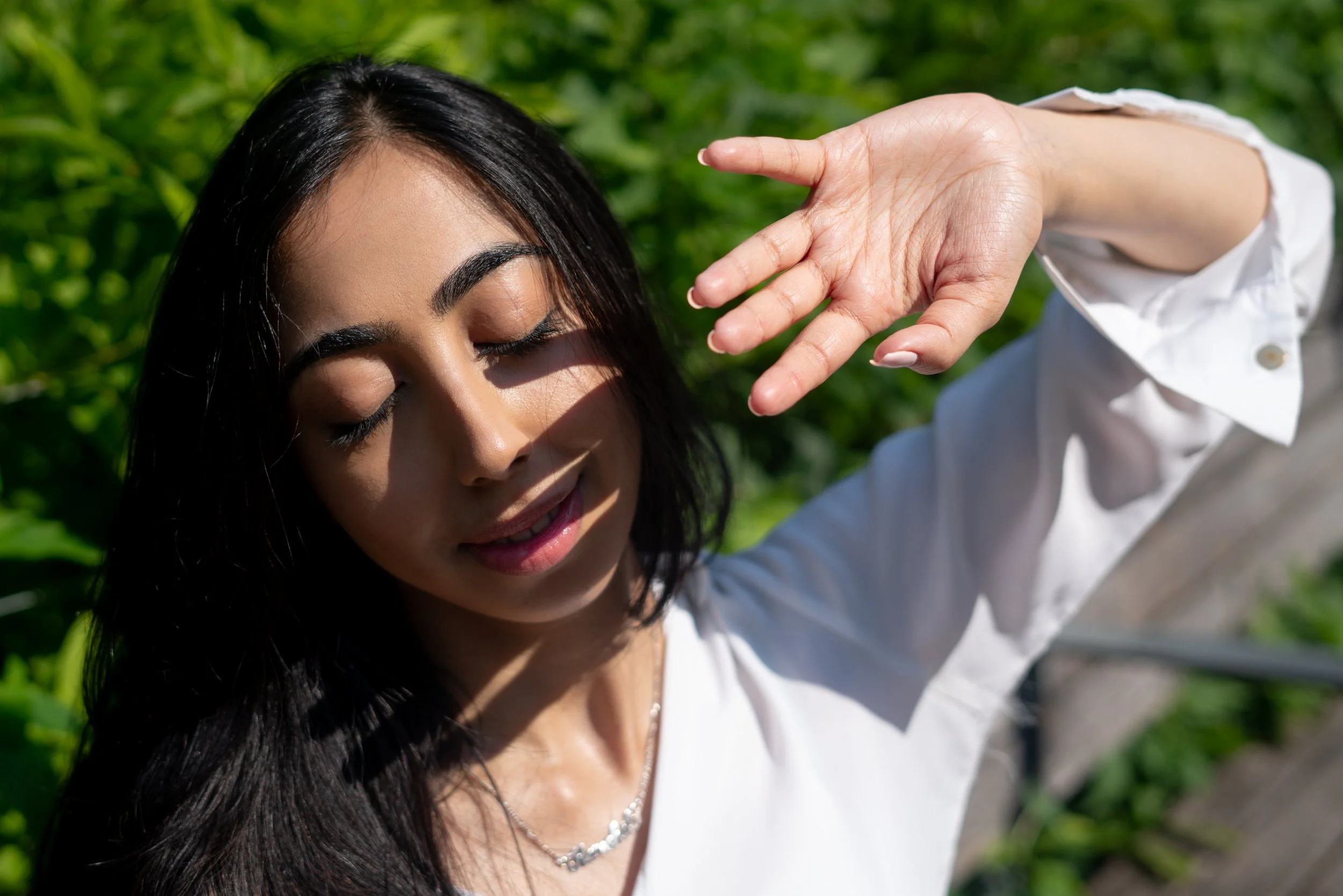 Natural light editorial close-up portrait of Harshita with soft shadows and greenery in the background