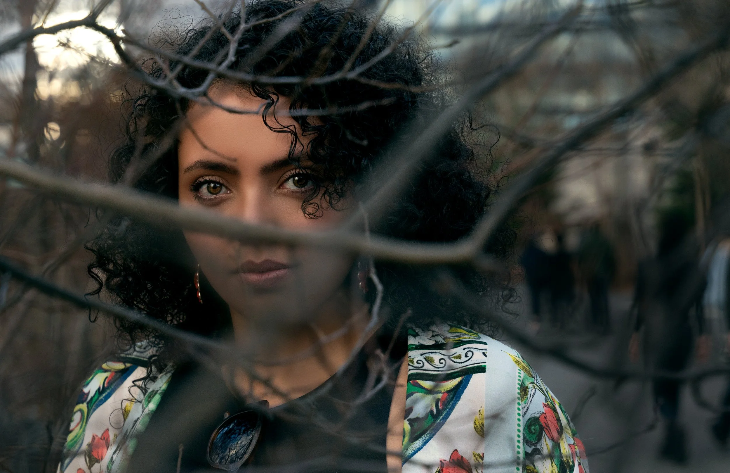 Close-up portrait of model framed through branches, creating a layered and intimate composition