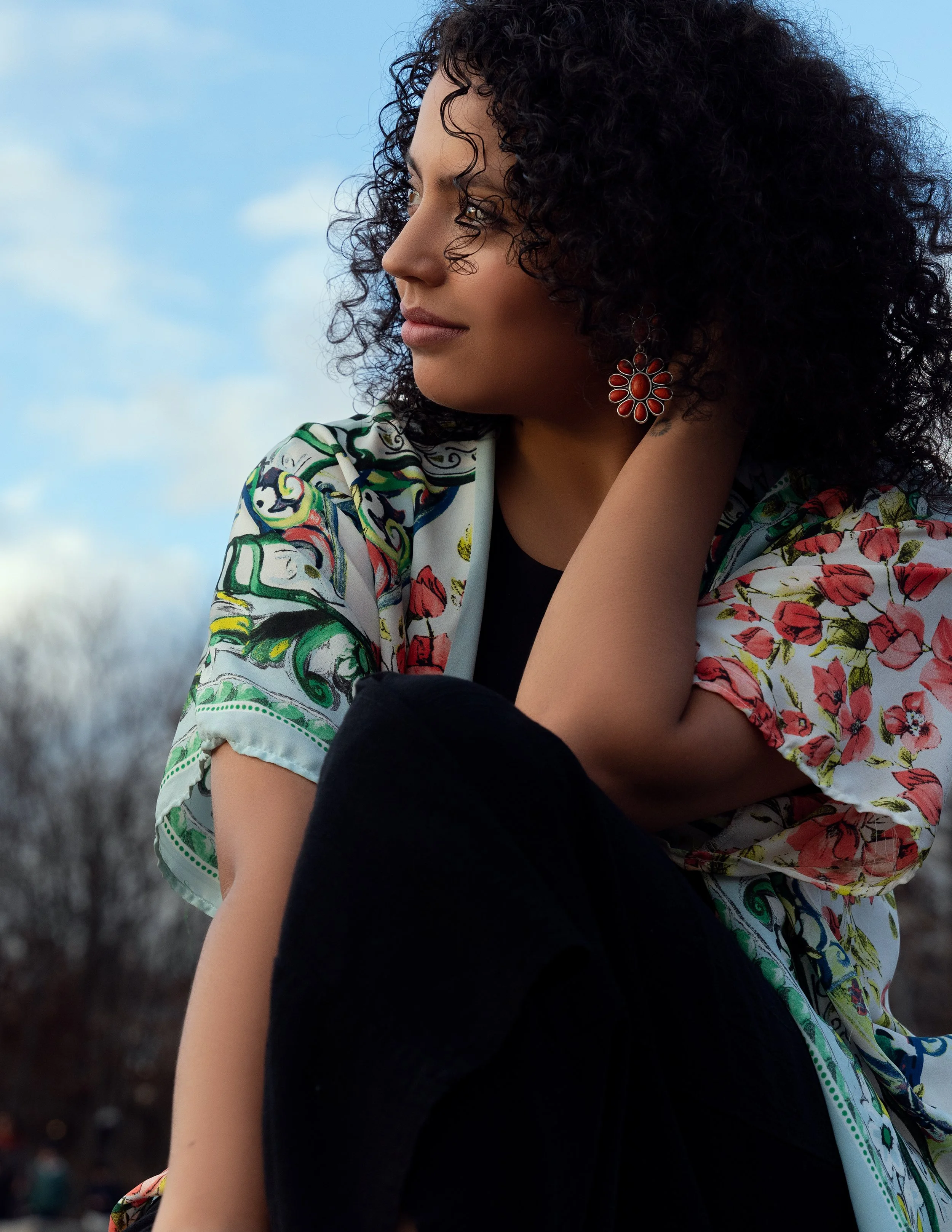 Curly-haired model in floral kimono looking sideways against a blue sky in natural light