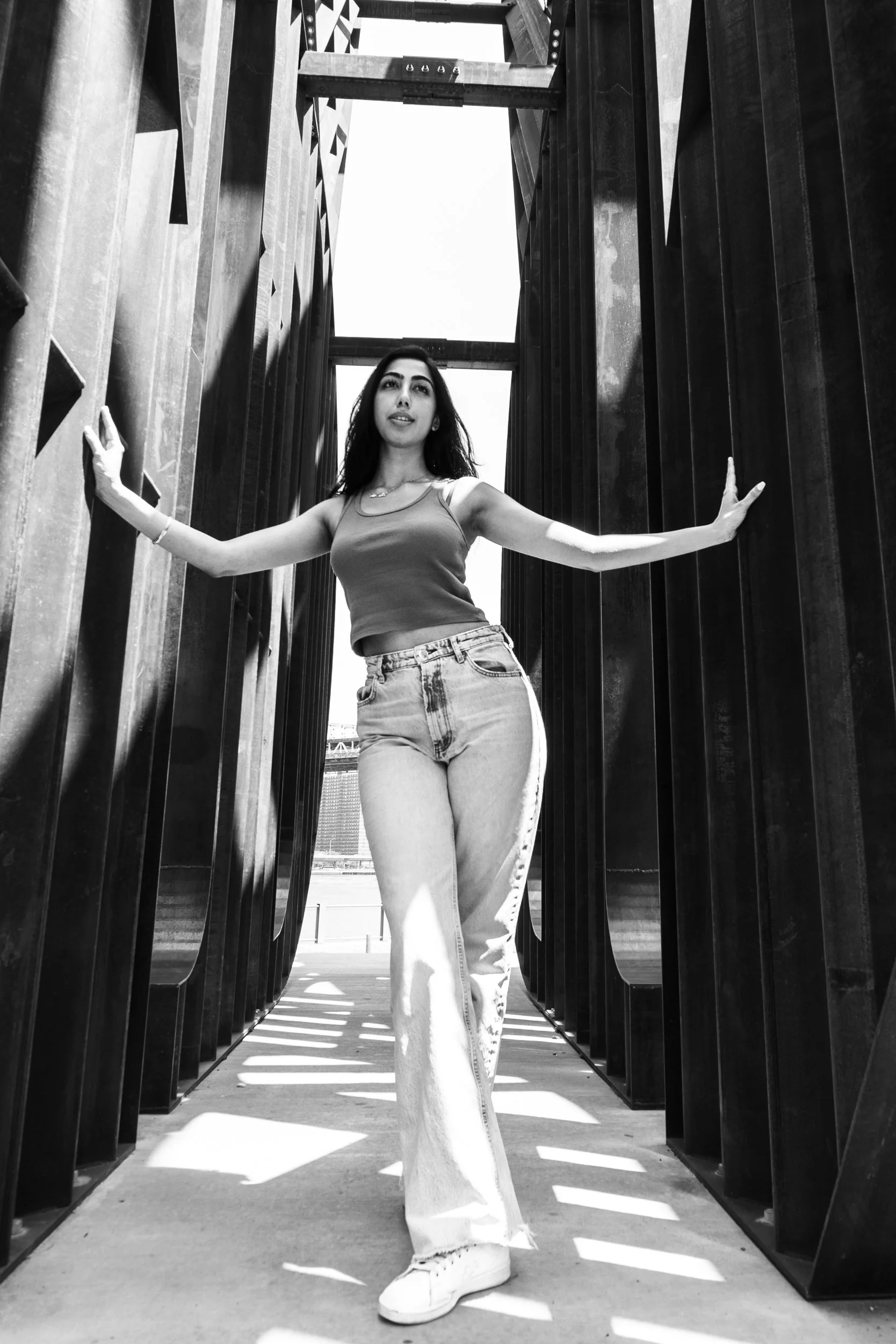 Black and white editorial portrait of Harshita standing between industrial steel beams in New York City