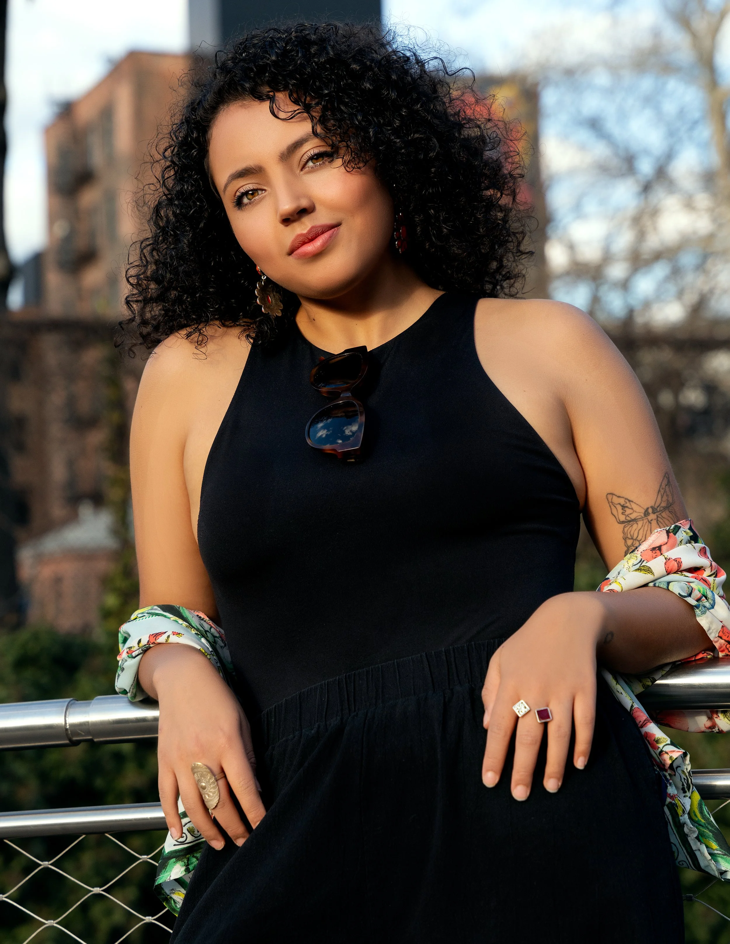 Portrait of model in black dress with floral kimono, standing by railing in warm natural sunlight