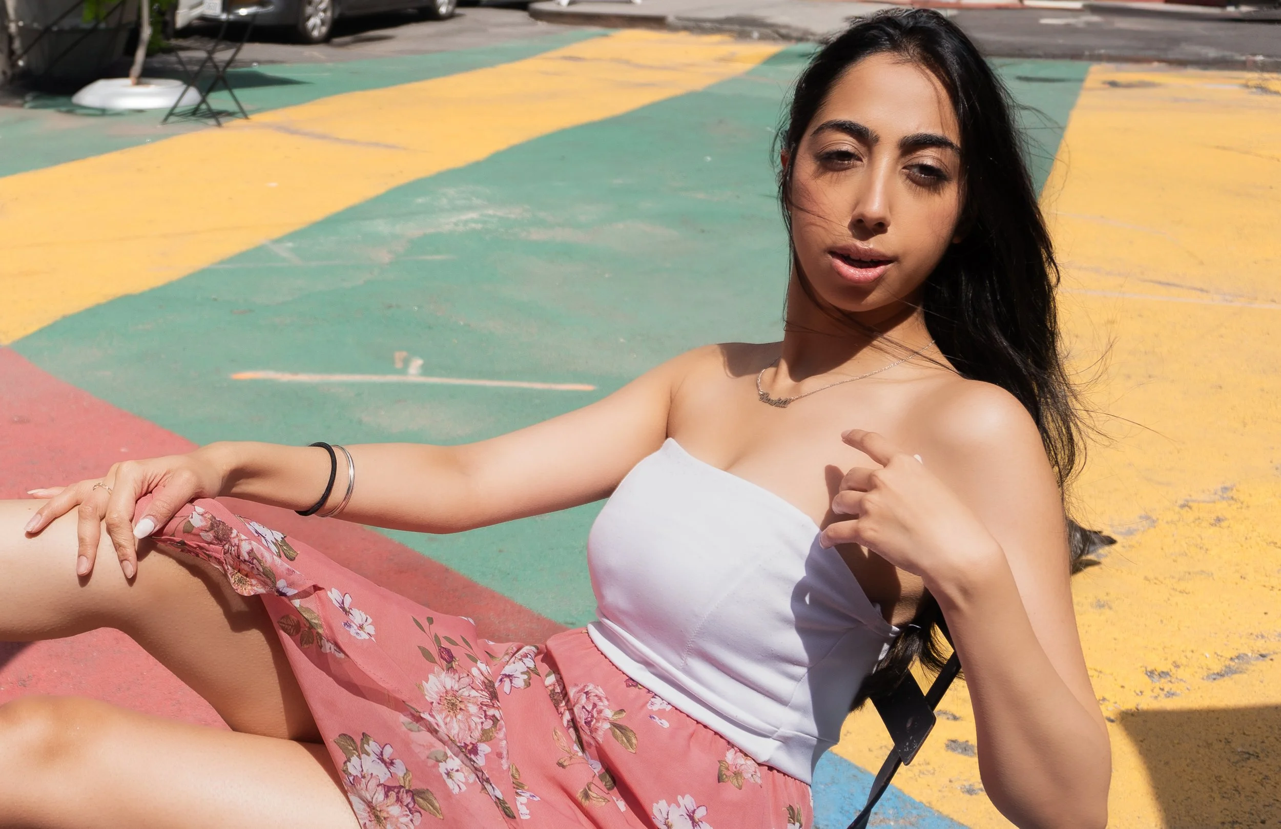 Editorial fashion portrait of Harshita sitting on a colorful street surface in bright sunlight in NYC