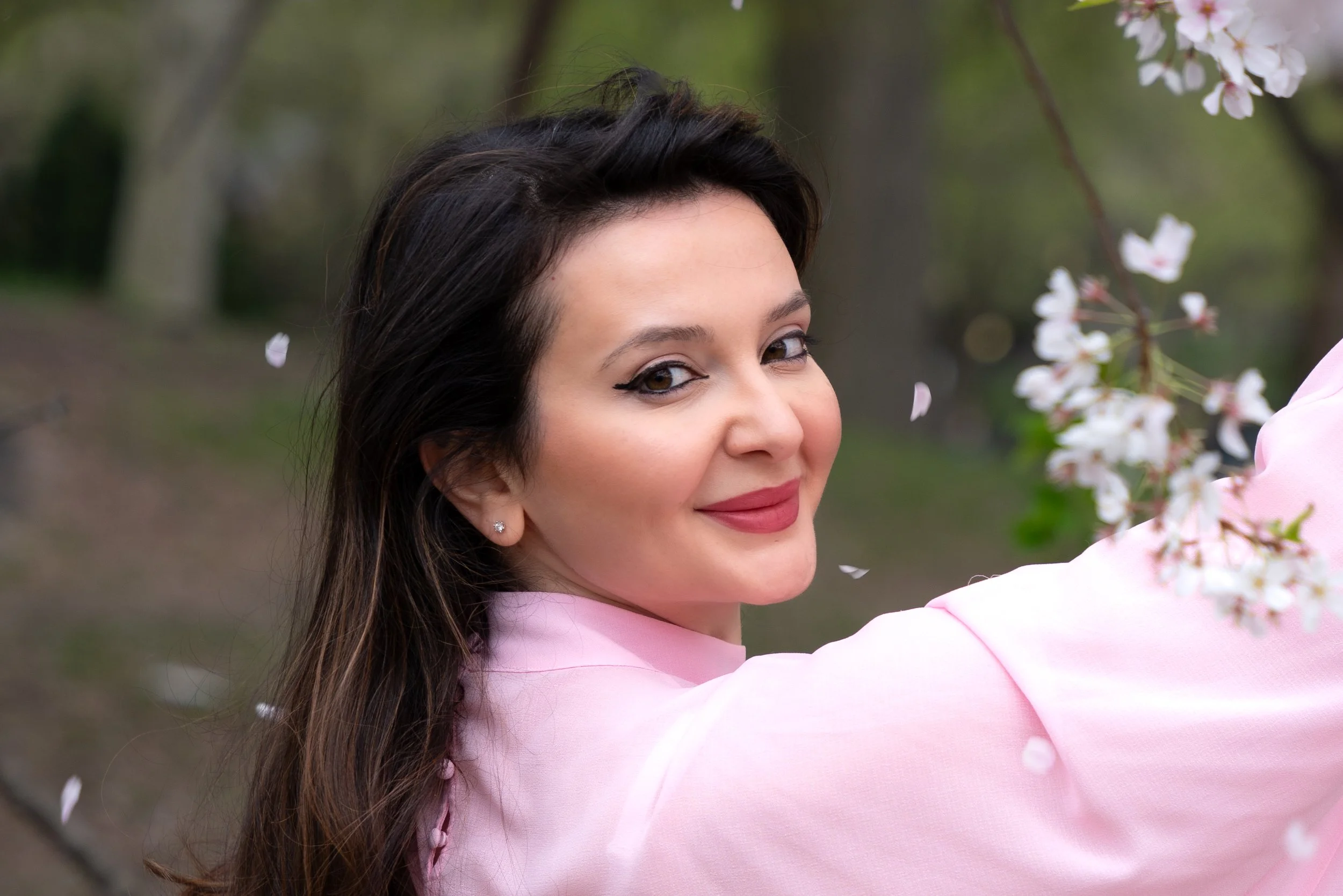 Silvia smiling in an editorial portrait surrounded by falling cherry blossom petals in Central Park, New York City