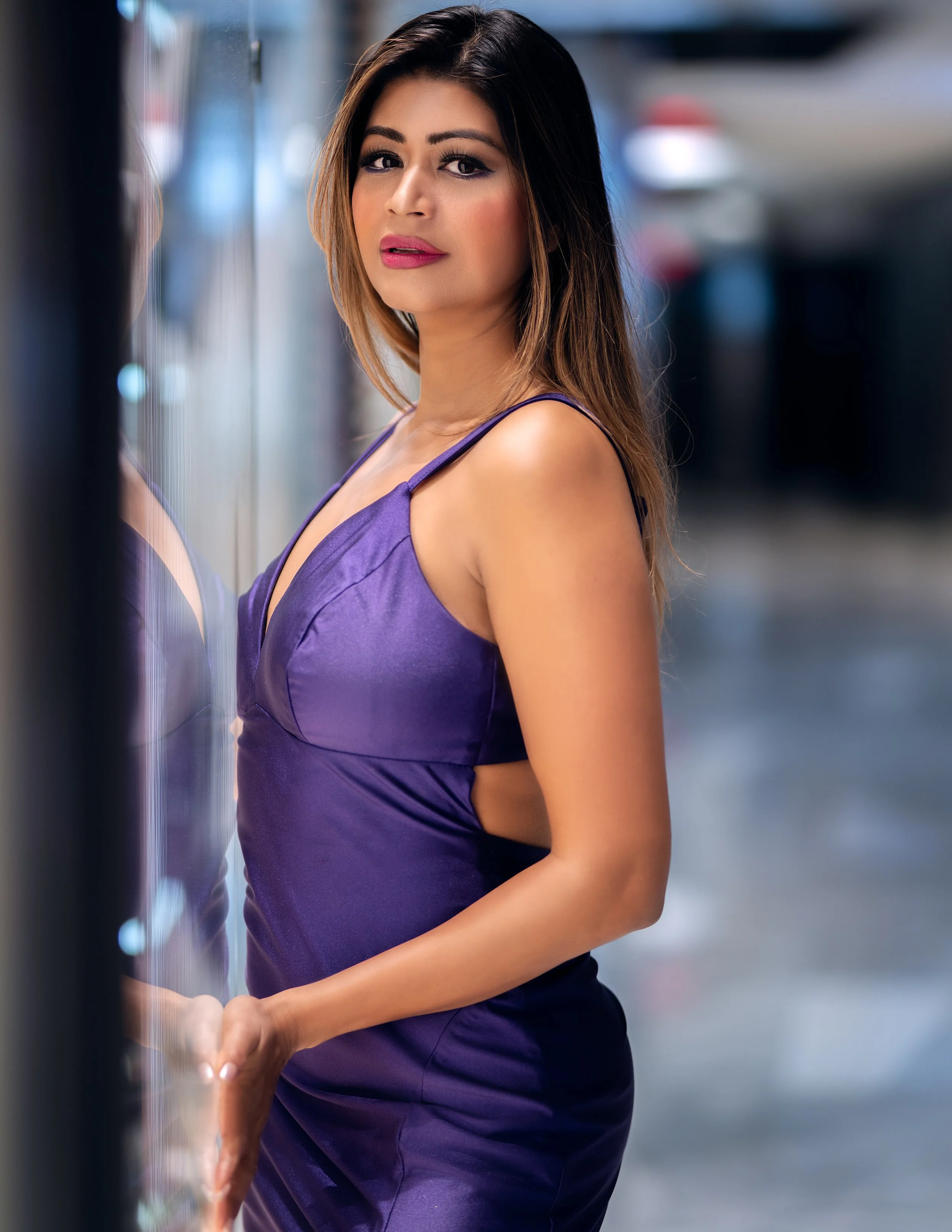 Editorial portrait of Yesmin in a purple dress standing by a glass wall with soft city reflections in NYC
